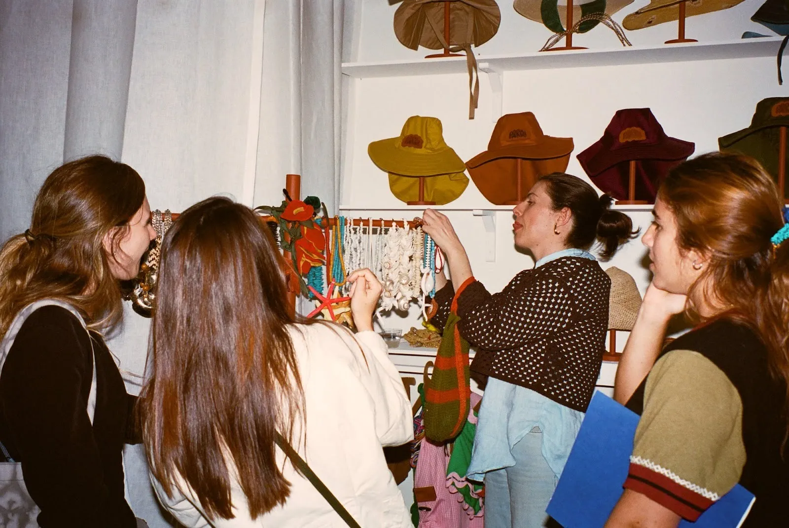 Latin American women picking out raffia hats at the opening night of SUDESTADA's exhibition in dreams we trust, Argentine fashion consultancy collaborating with artists, Gimena Garmendia.