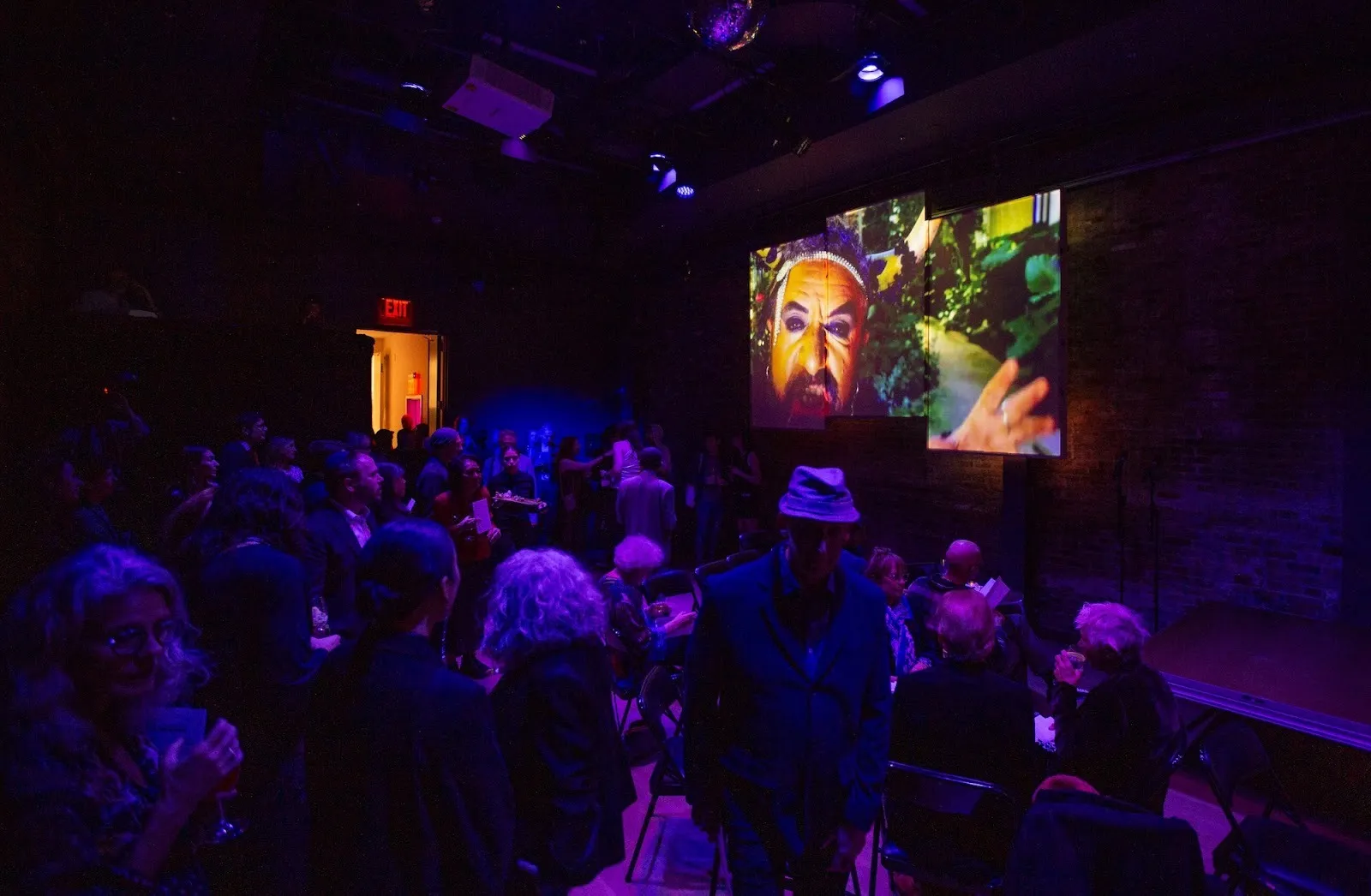 Partygoers watch artist Tareke Ortiz’s live-streamed performance in a dim room at La MaMa's 63rd anniversary benefit for experimental theater.