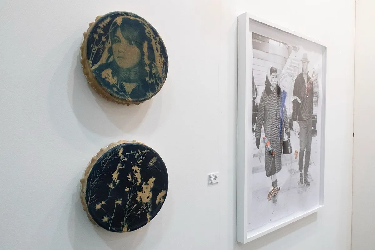 Gallery booth of ceremonial art gallery at art toronto 2024, two dreamy silhouetted cyanotype images layered atop elk hide drums, next to drawing on top of black and white photograph titled fireweed, work by michelle sound.