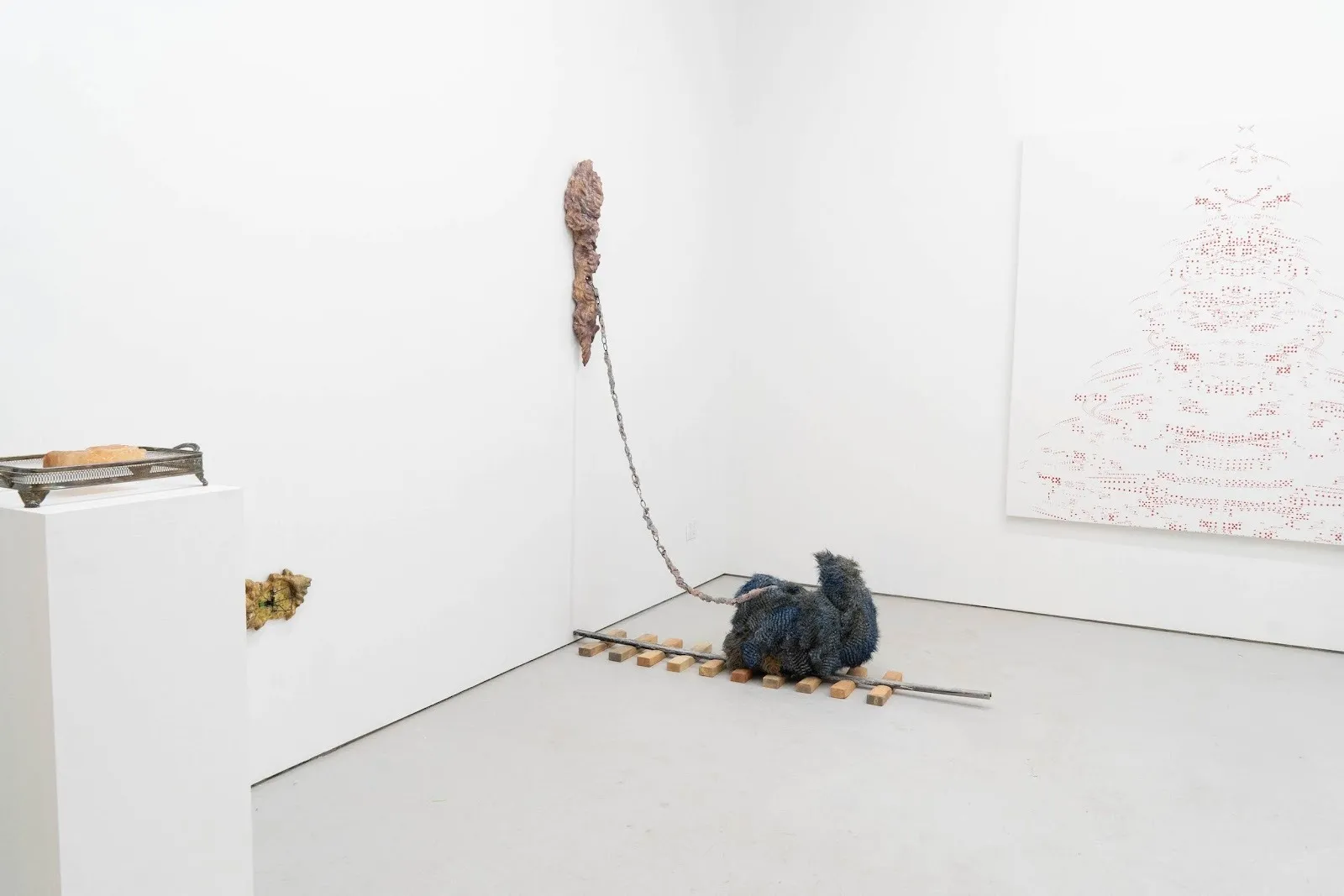 Installation view of furry sculpture chained to a wall mounted ceramic structure, white cube Gallery exhibition at will adaptations, Echo Youyi Yan, Axial Domestication.