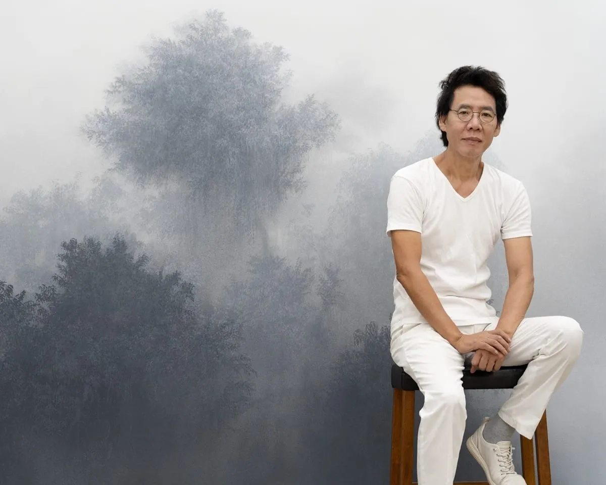Korean artist wearing white T-shirt and white jeans sitting in front of his painting, Misty grayscale natural landscape paintings installation view in white cube gallery wall, Tina Kim, there is no place, Kibong Rhee exhibition.
