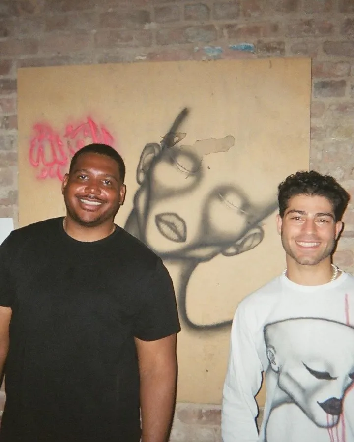 Two make artists standing in front of Rubeen Salem's work on a brick wall, palestinian artist figurative drawing and paintings.