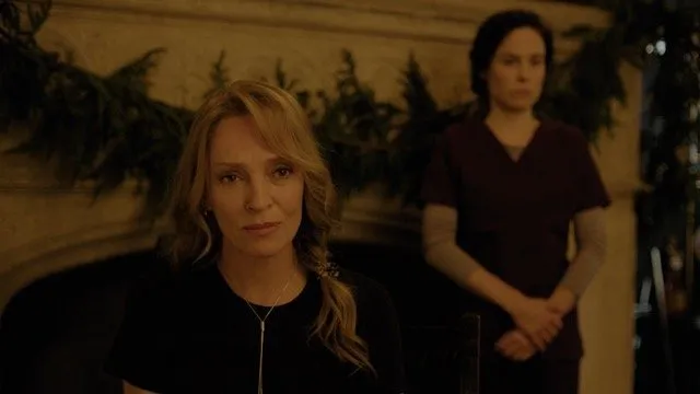 Two women (with Uma Thurman with blond hair) standing in front of fireplace in dark living room, looking solemn, still from Oh, canada by paul schrader.