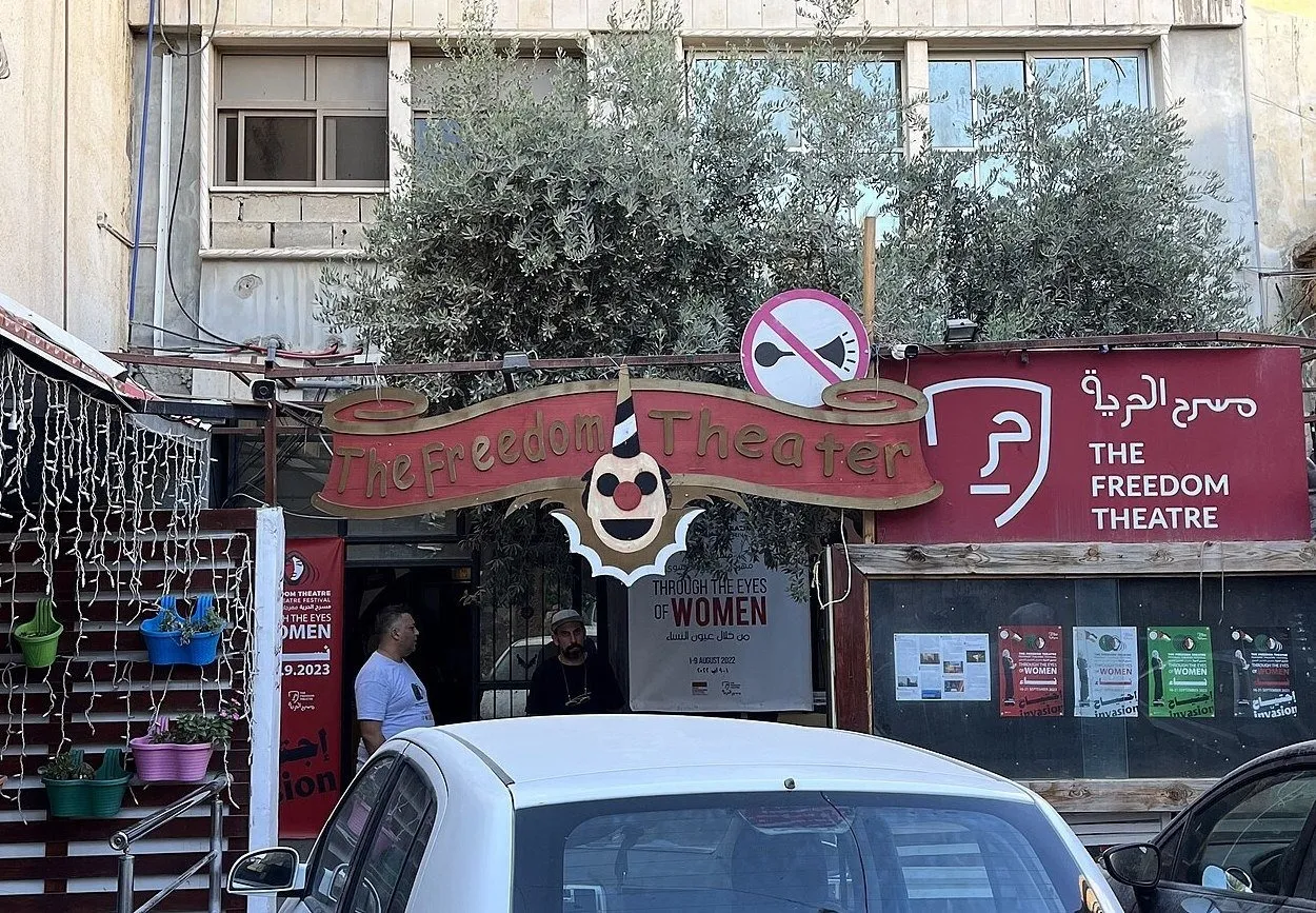 Entrance of the Freedom Theatre at the Jenin refugee camp, in the city of Jenin, Palestine, neighborhood floor-level door with red theater symbol and no honking sign on top.