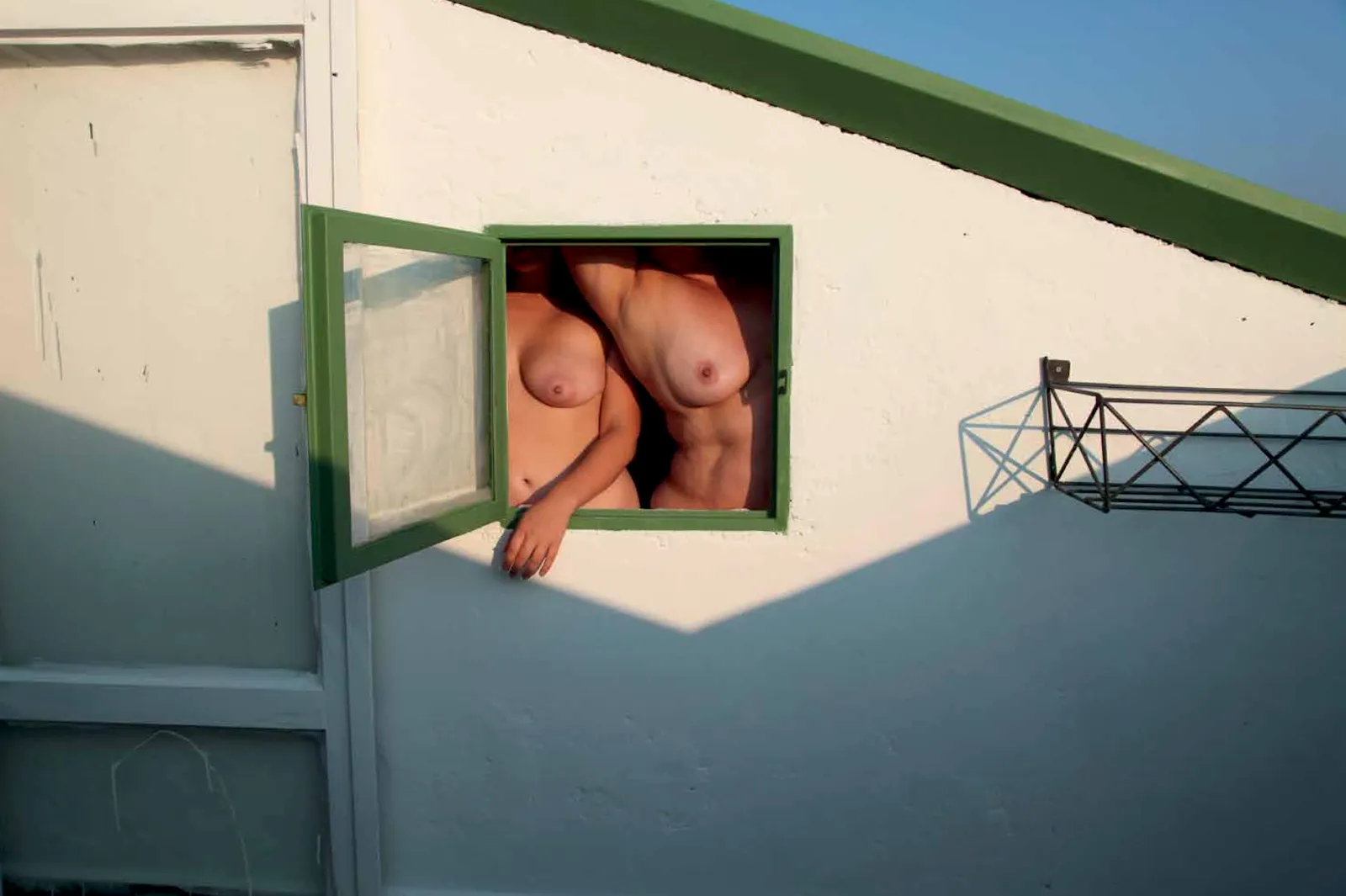 Two female nude bodies in green window framed by white wall, intimate photography by Jeanette Spicer from the series to the end of the earth.