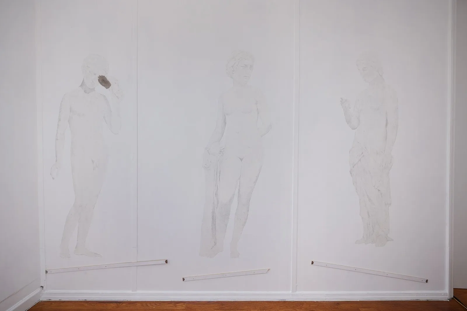 Three life-sized ghost-like graphite figures floating atop yardsticks mounted on gallery wall, conduct exhibition at iowa gallery by artist hunter foster.