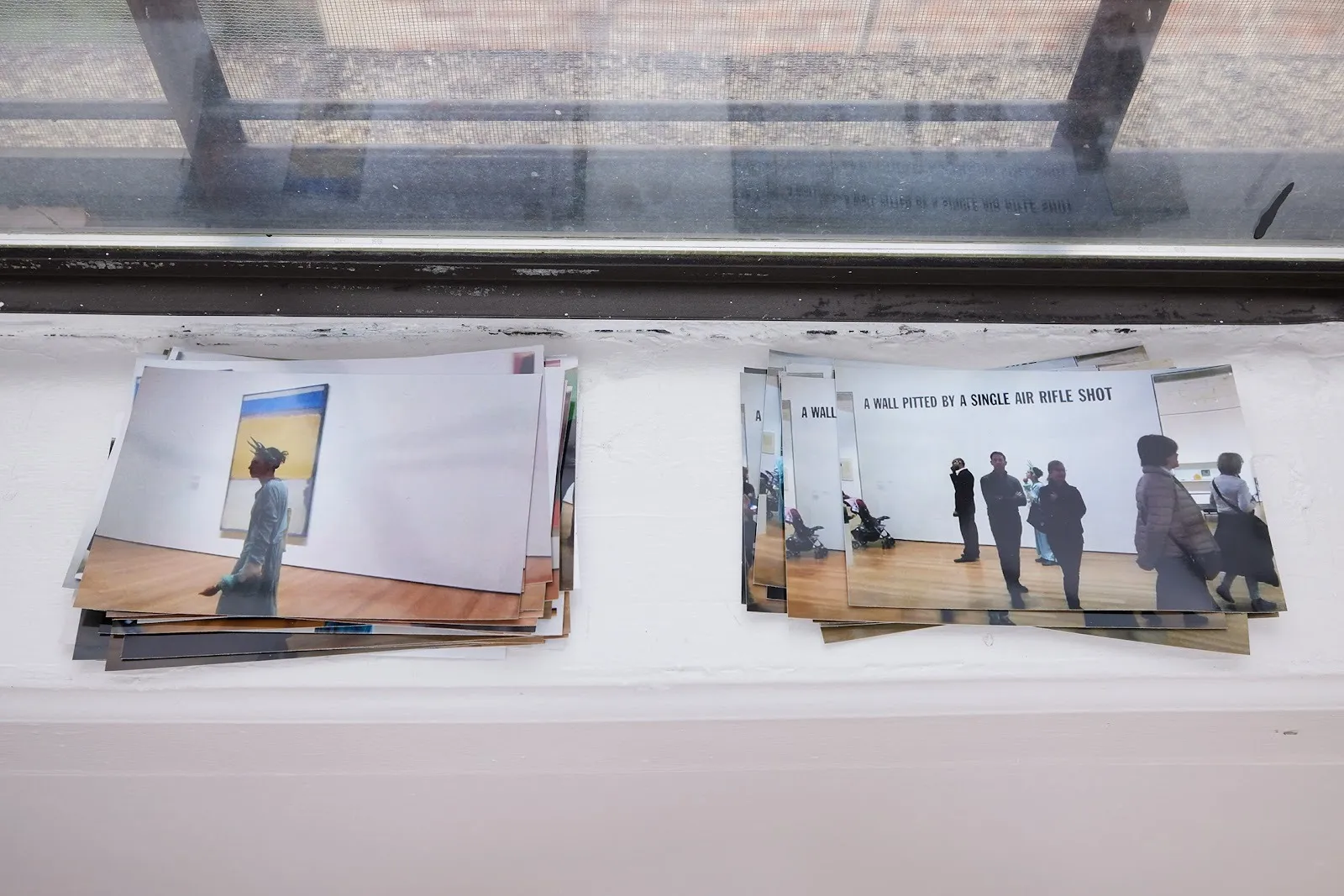 Stacks of photos on a window sill as part of conduct at iowa gallery, dana de giulio realism for the cause of future revolution, unauthorized performance at the museum of modern art in gallery space to transgress institutional boundaries.