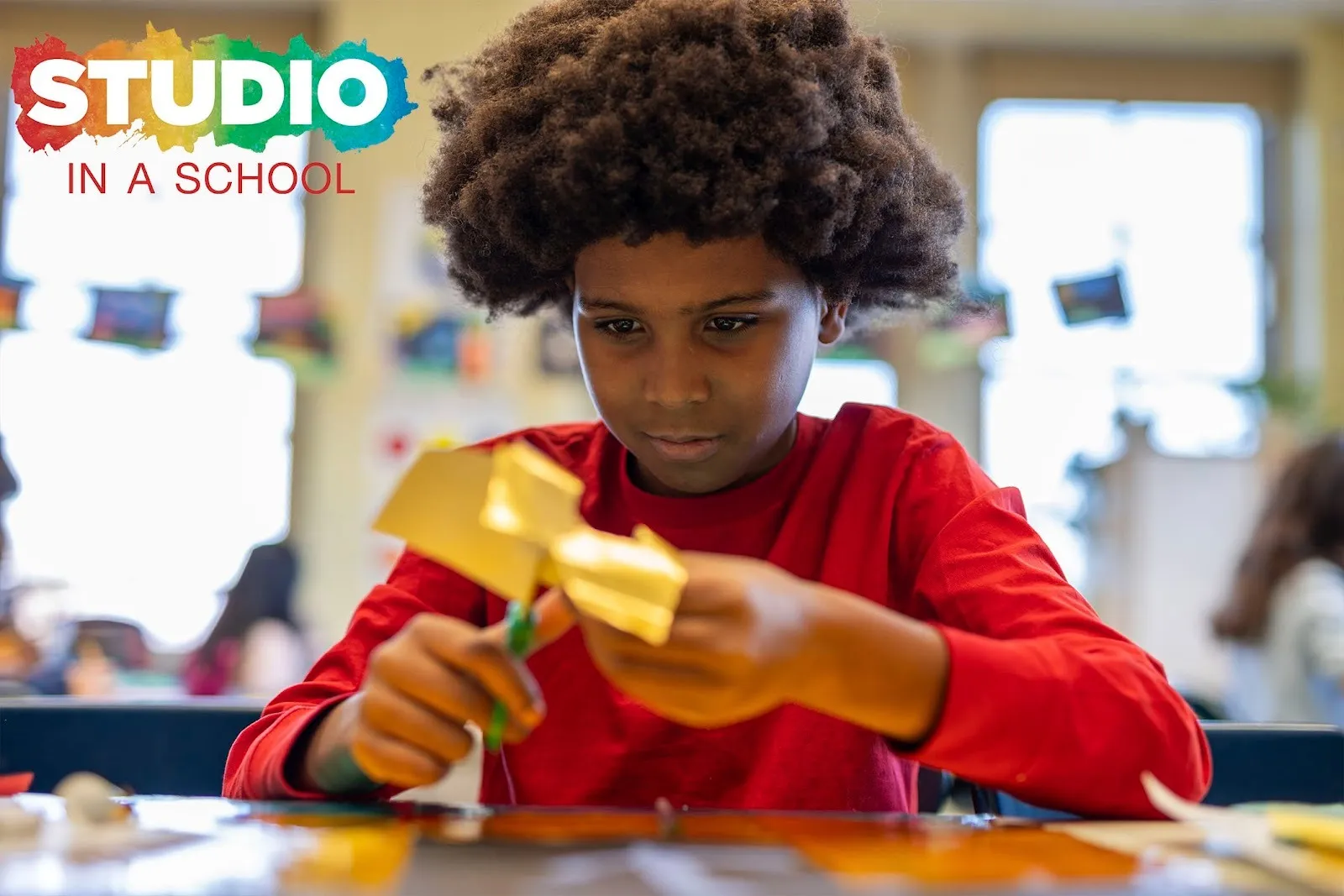 Fifth grade boy learning how to make papercuts wearing red shirt, ps 72 the bronx, studio in a school educational nonprofit, mural project with james Reynolds, interview with hasna muhammad.