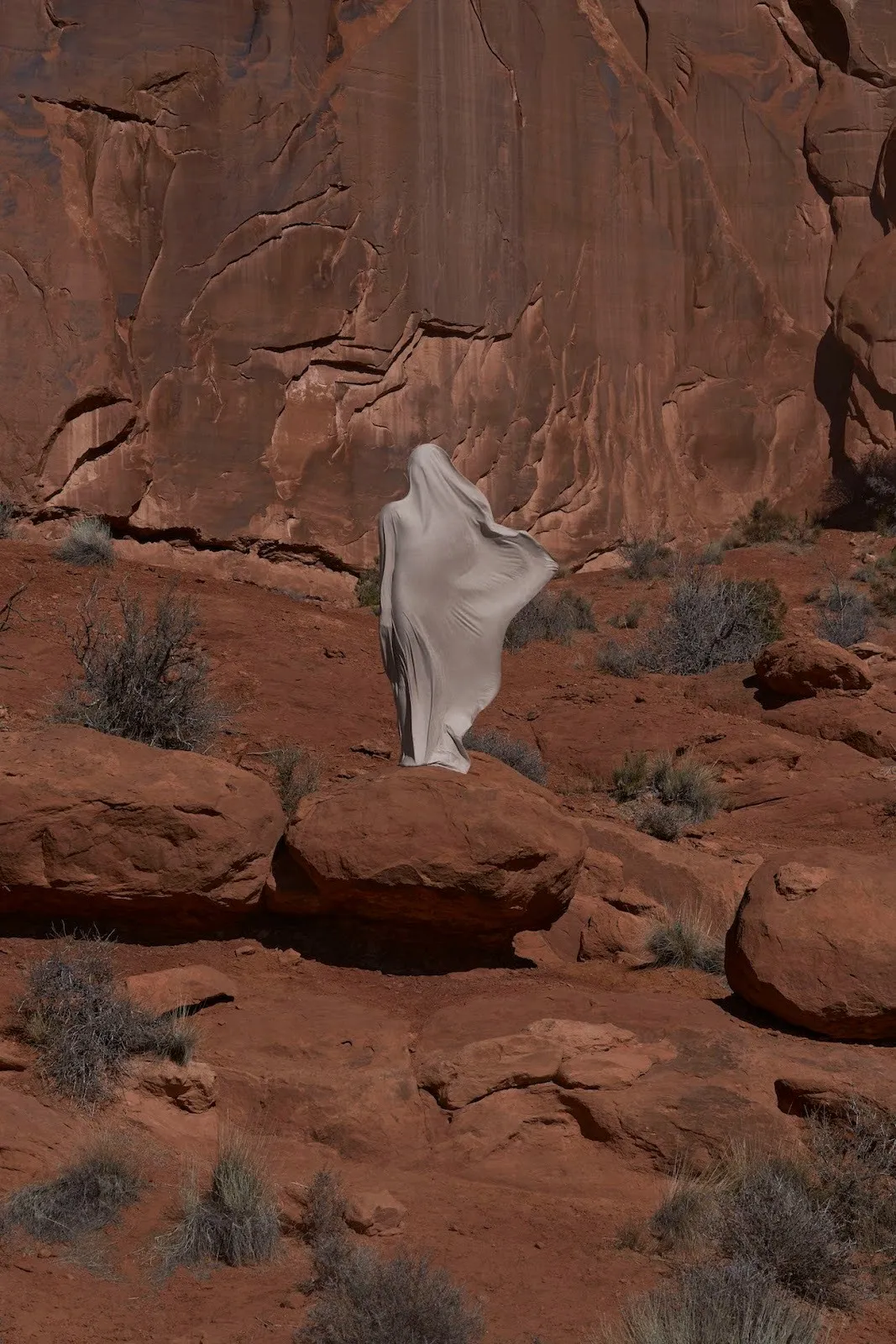 Juan Sebastian, Espejo, 2021 photograph of veiled figure walking in desert next to monolithic huge Stone by Colombian immigrant artist.