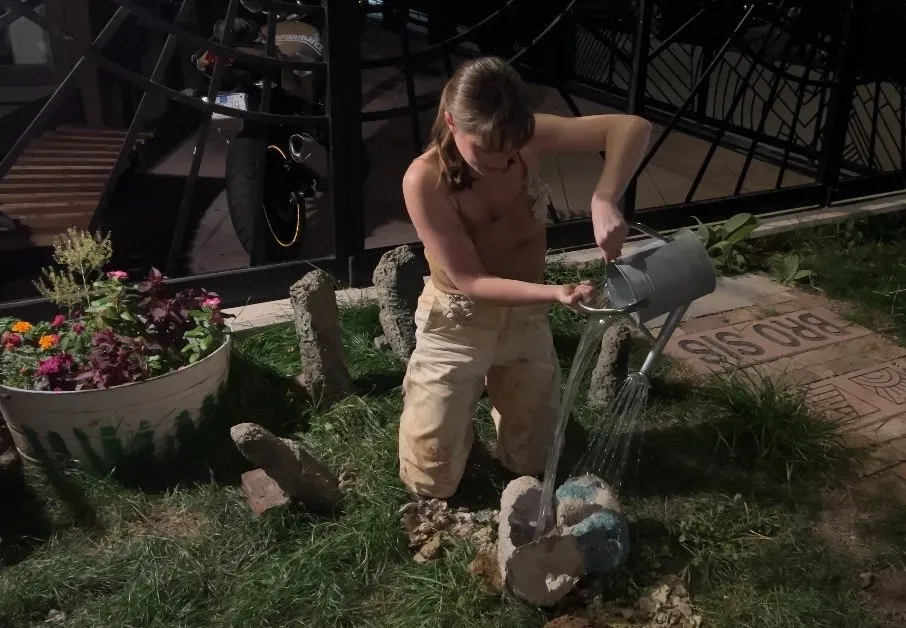 Garden of voices performer wearing beige and white costume watering in the garden, collaboration between project iii and embodied earth, interview with nicole jackson and kasey broekema.