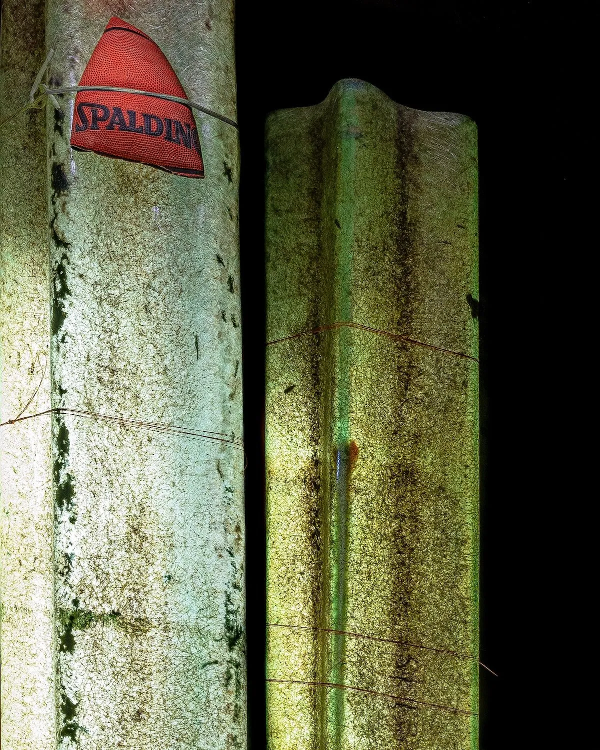 Bronzy green installation with flattened basketball, sculptural artwork by Filippo Vogliazzo, detail of Light Sleepers photographs by Jorge Villarreal, Casa Caché artist residency.