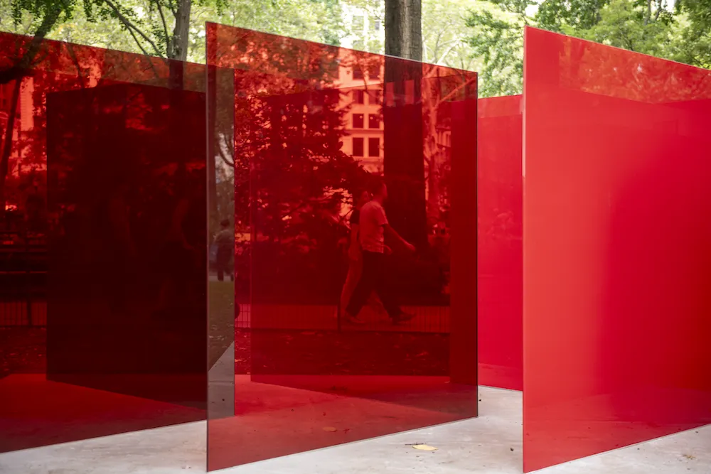 Layers of deep red glass panels create a reflective, maze-like interior with faint silhouettes of park visitors.