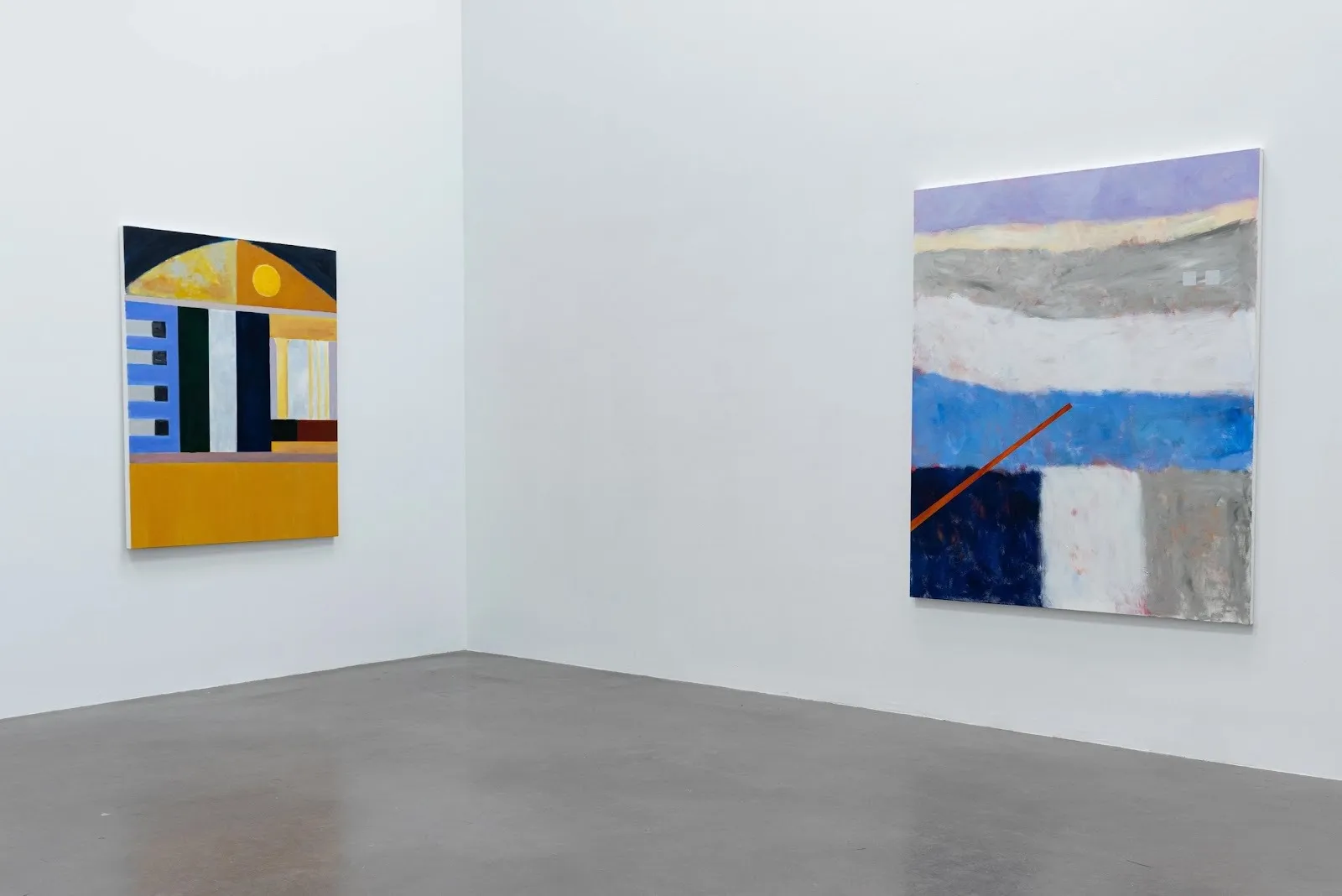 Two abstract paintings hang in a corner: one in mustard yellow and blue geometric forms, the other with layered horizontal bands of soft blues and grays crossed by an orange line.