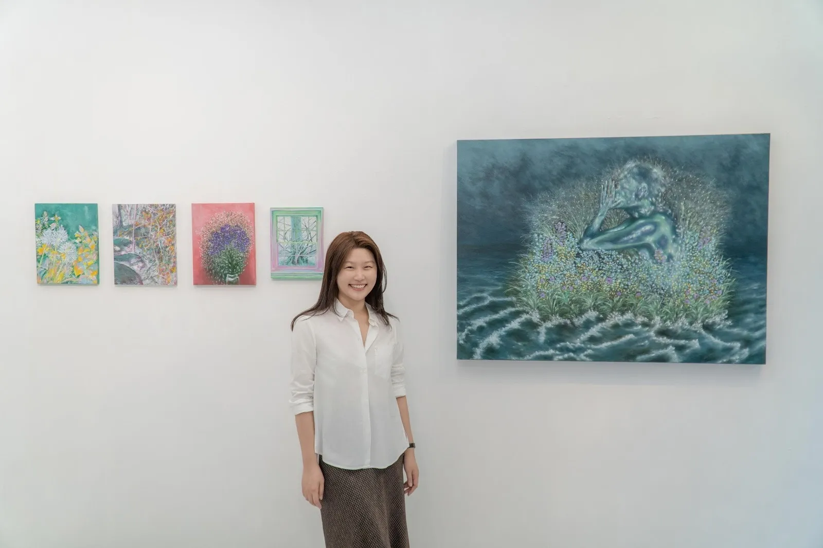 South Korean curator Irene Gong smiling happily in front of Kimin Kim's blue and green plant paintings.
