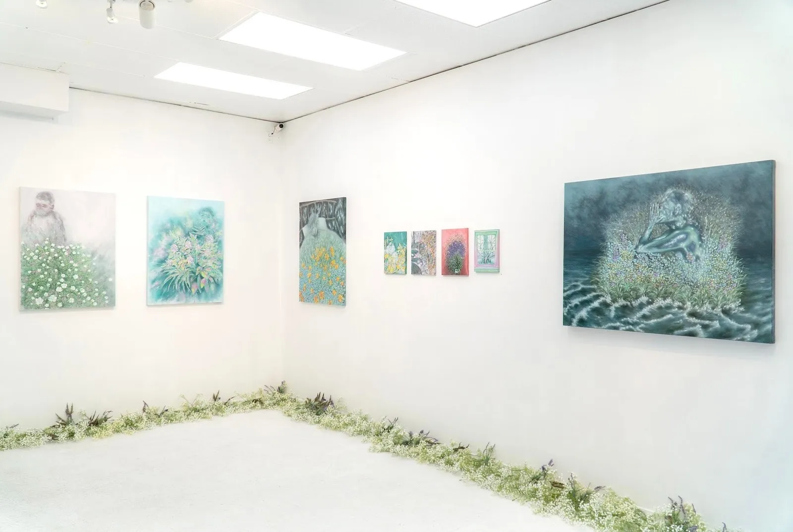 Kimin Kim's green and blue plant paintings hanging in a gallery curated by Irene Gong, grass growing along the wall.