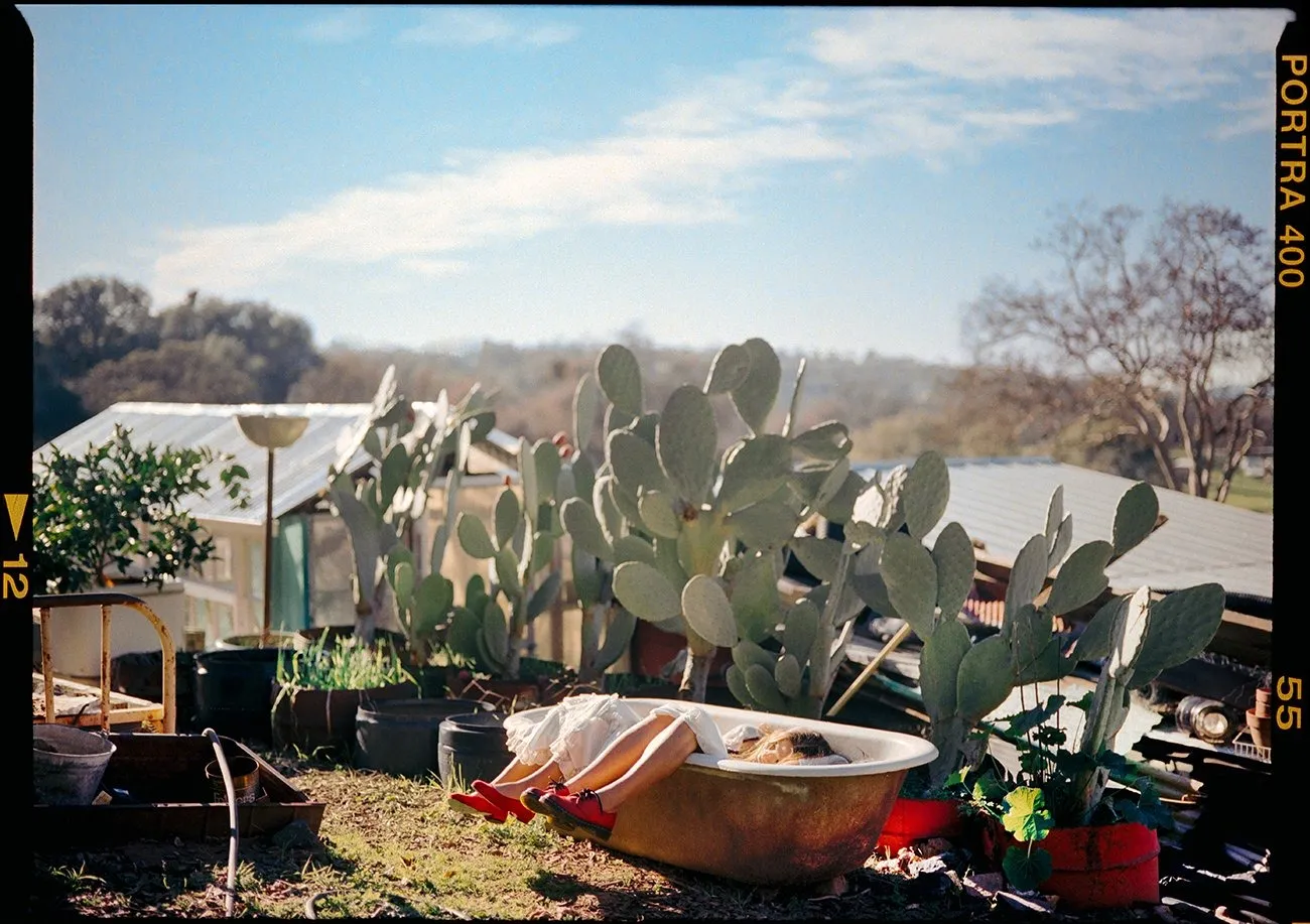 Analog photo on Portra of two girls lying in bathtub on desert with cactus and tents behind them, photographers Amber Maalouf and Ashlie Chavez.