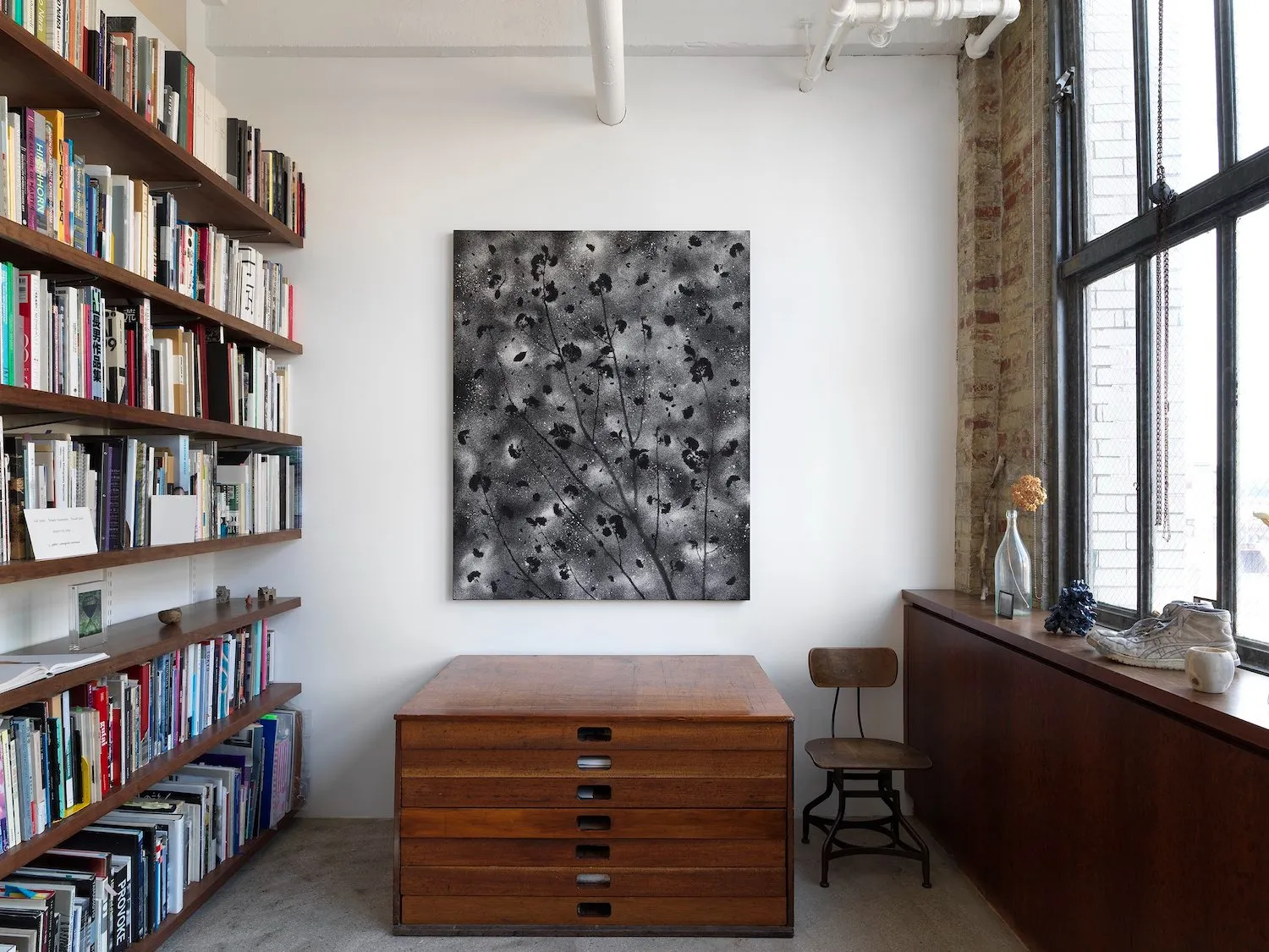Installation view of Motohiro Takeda: Something To Remember You By at Alison Bradley Projects, charcoal flower abstract black and white painting and random memorabilia on window sill, bookshelf on the left in office-like setting.
