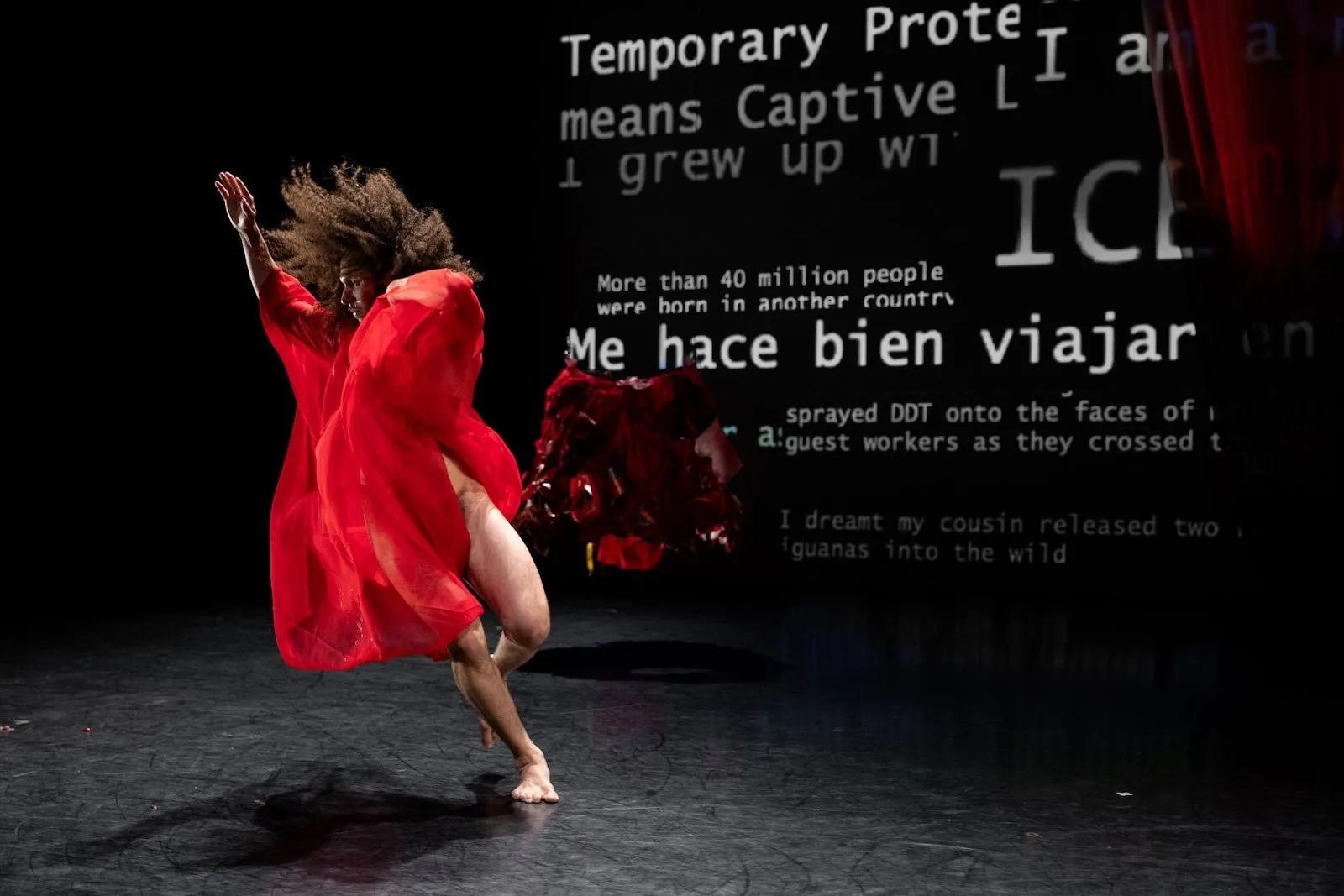 Miguel Alejandro Castillo, latin man with dark hari dancing in red dress in front red rose and text projection saying "me hace bien".