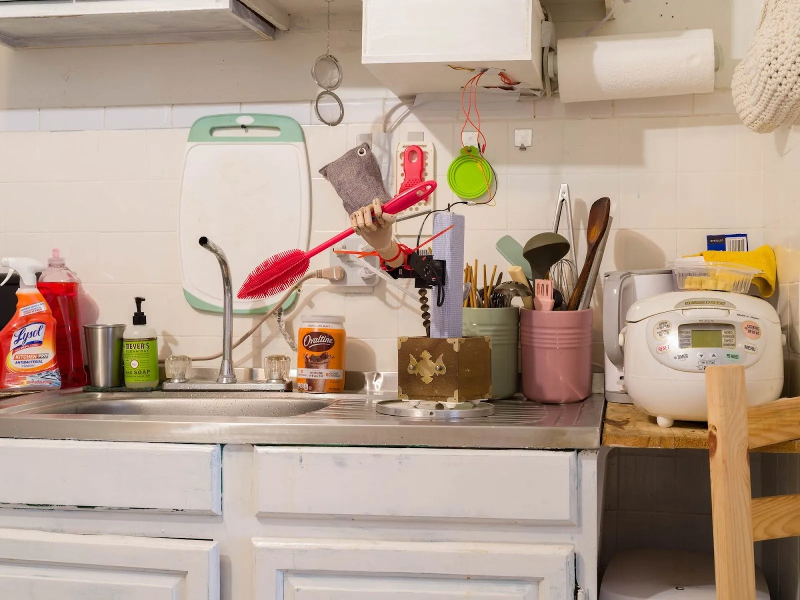 Messy kitchen counter with mannequin hand holding cooking utensils as art installation by Elaine Xuhong Chen, Bandaged Moments at Tutu Gallery.
