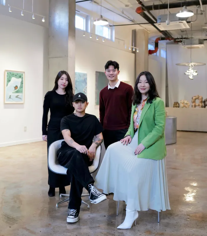 The curatorial team of bios, morphe (from left: Minju Kim, Ho Jae Kim, Sean Zhang, Lucy Liu), four young Asian curators in professional attire sitting in gallery.