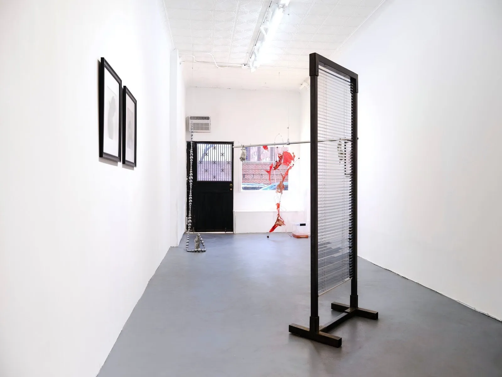 White cube gallery with faux window blinds, posthuman mannequin photos, blood circulation installation, hanging pewter beam with two hands, bleach cannisters, installation view of group exhibition peripheral belonging at ghostmachine.