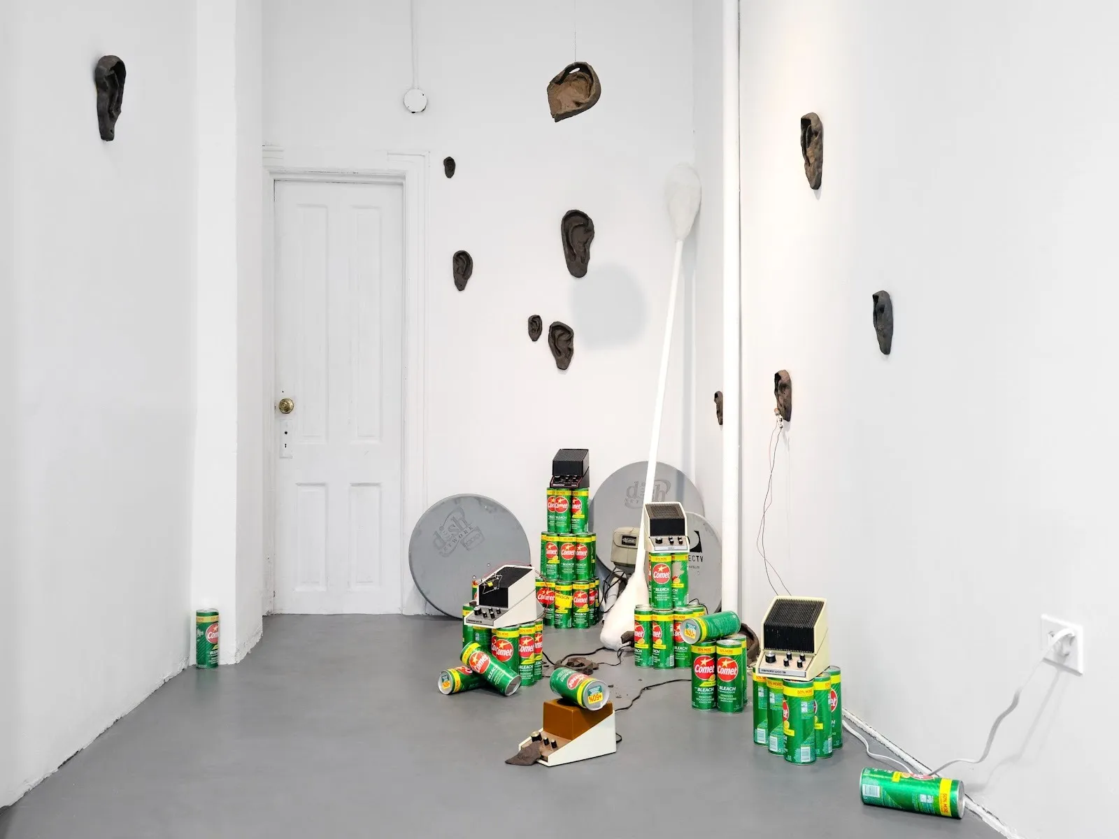 Green bleach cannisters stacked on floor with Marsona sleep aids noise machine, circuits, Black ears and sattelite dishes in white cube gallery, Char Jere, peripheral belonging group show at GHOSTMACHINE.