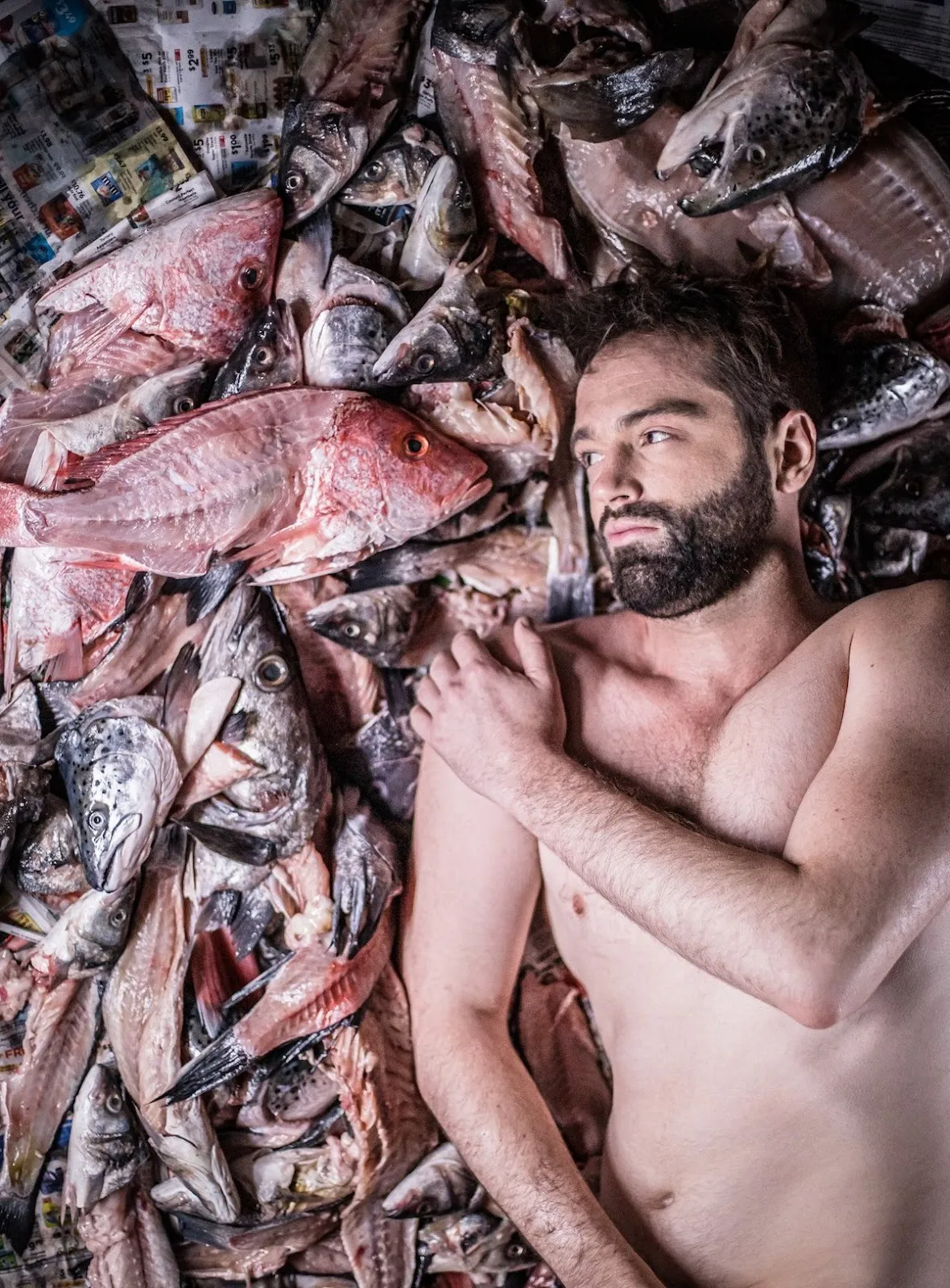 Naked men with beard lying in a pile of dead fish, immersive insulation photograph projection, the fabric workshop and Museum Philadelphia, John Jarboe gender journey.