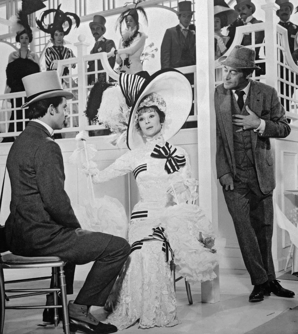 Still from 1964 my fair lady, eliza doolittle sitting at upper class gathering, featuring audrey hepburn, rex harrison, and jeremy brett, impulse magazine film review by tiffany babb.