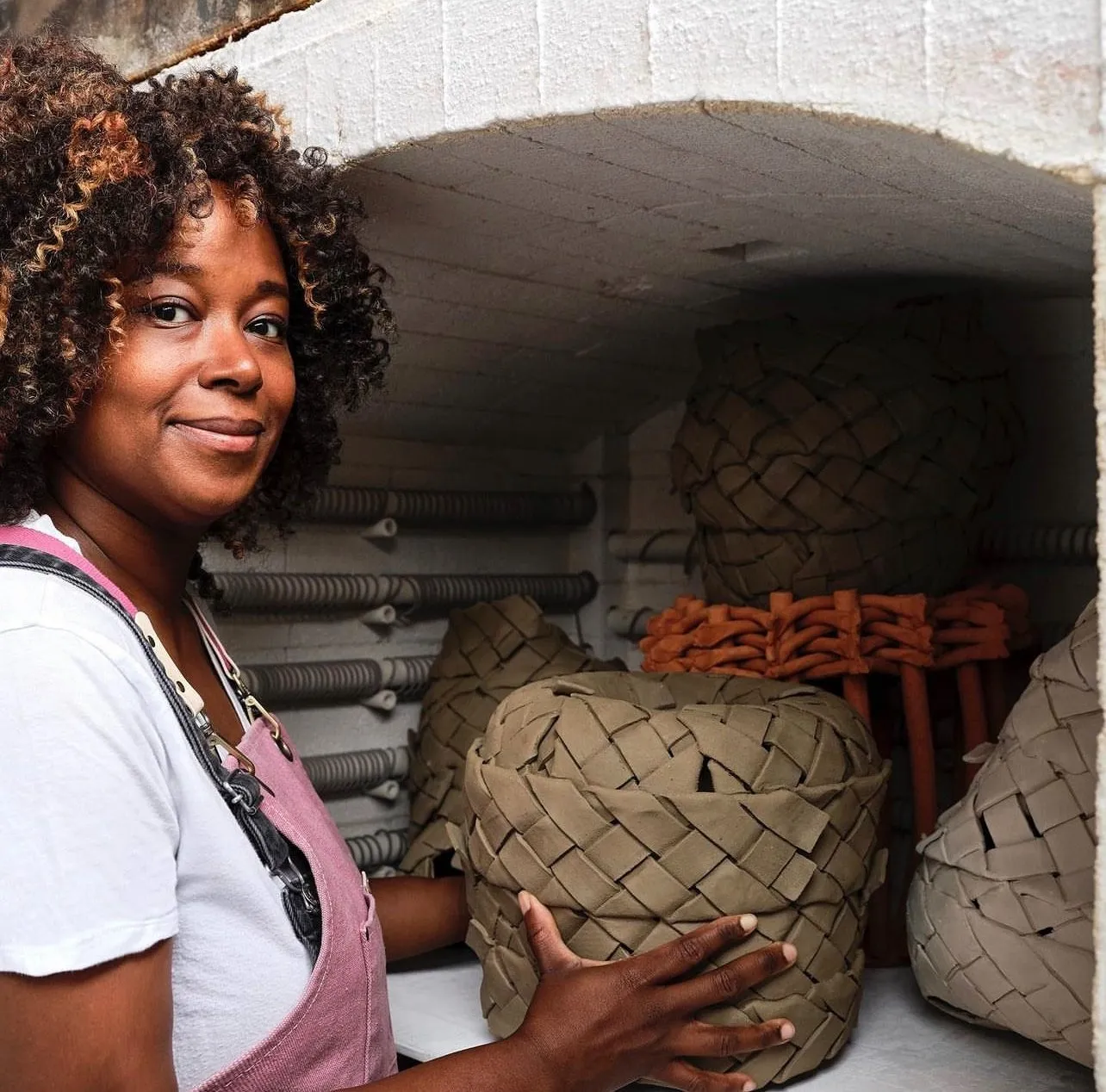 Bahamian artist holding woven clay pot and putting it into urn, Studio portrait of Anina Major impulse magazine interview with jenny wang.