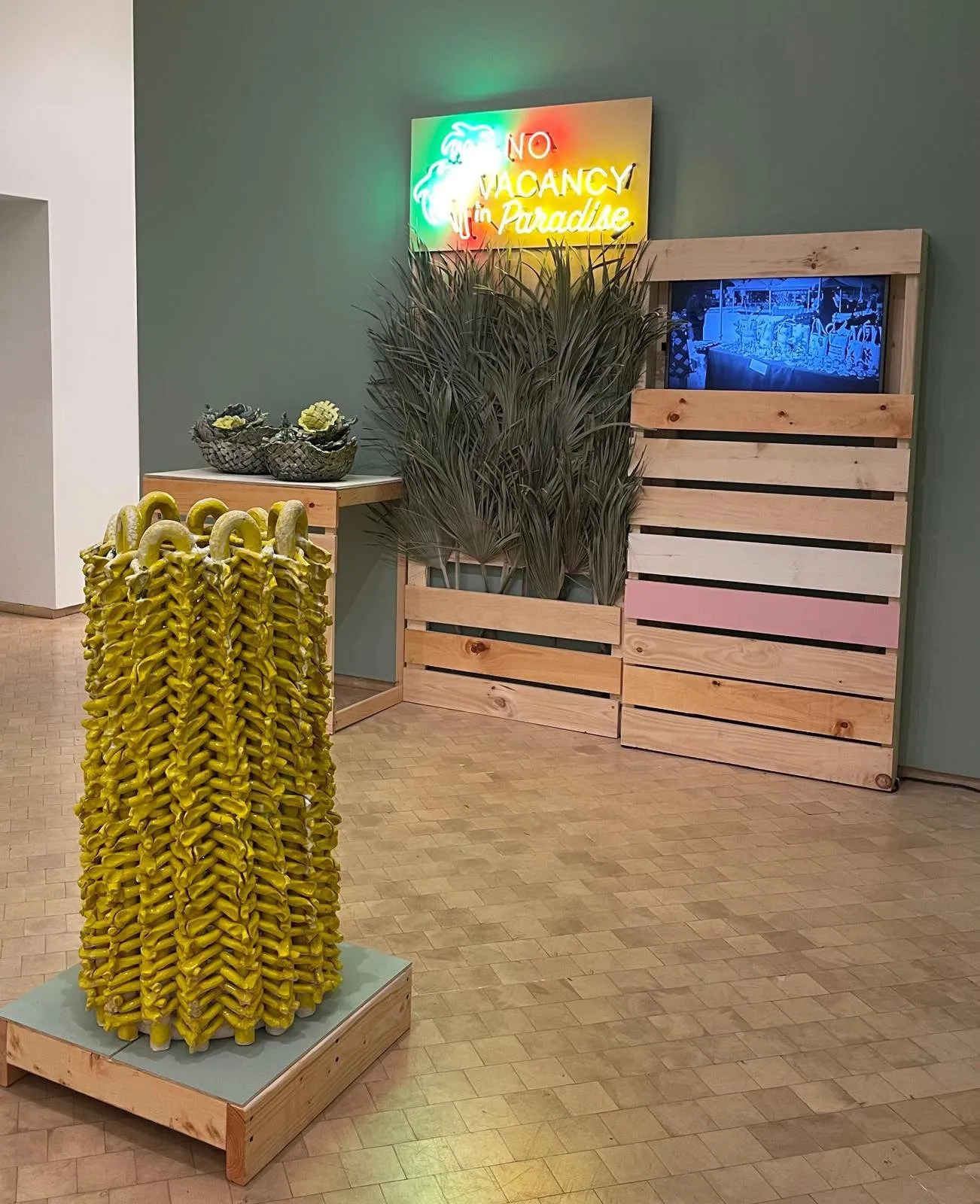 Woven clay pile with yellow accents in front of wooden crates with straws for sale, Bahamas Street market installation, neon light plates that reads, no Vacancy in Paradise, el museo del barrio, Anina Major impulse magazine interview with jenny wang.