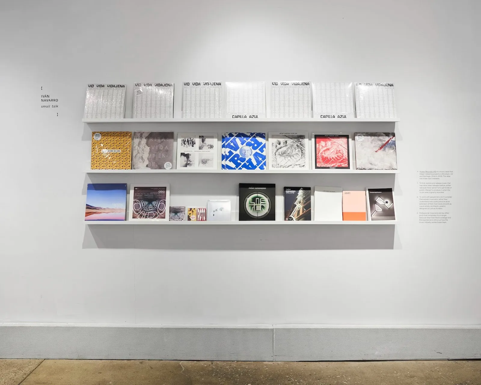 Three tiered shelves with posters, zines and books, installation view of Iván Navarro solo exhibition Small Talk at Miriam Gallery, chilean political art reviewed by emma jones, impulse magazine.