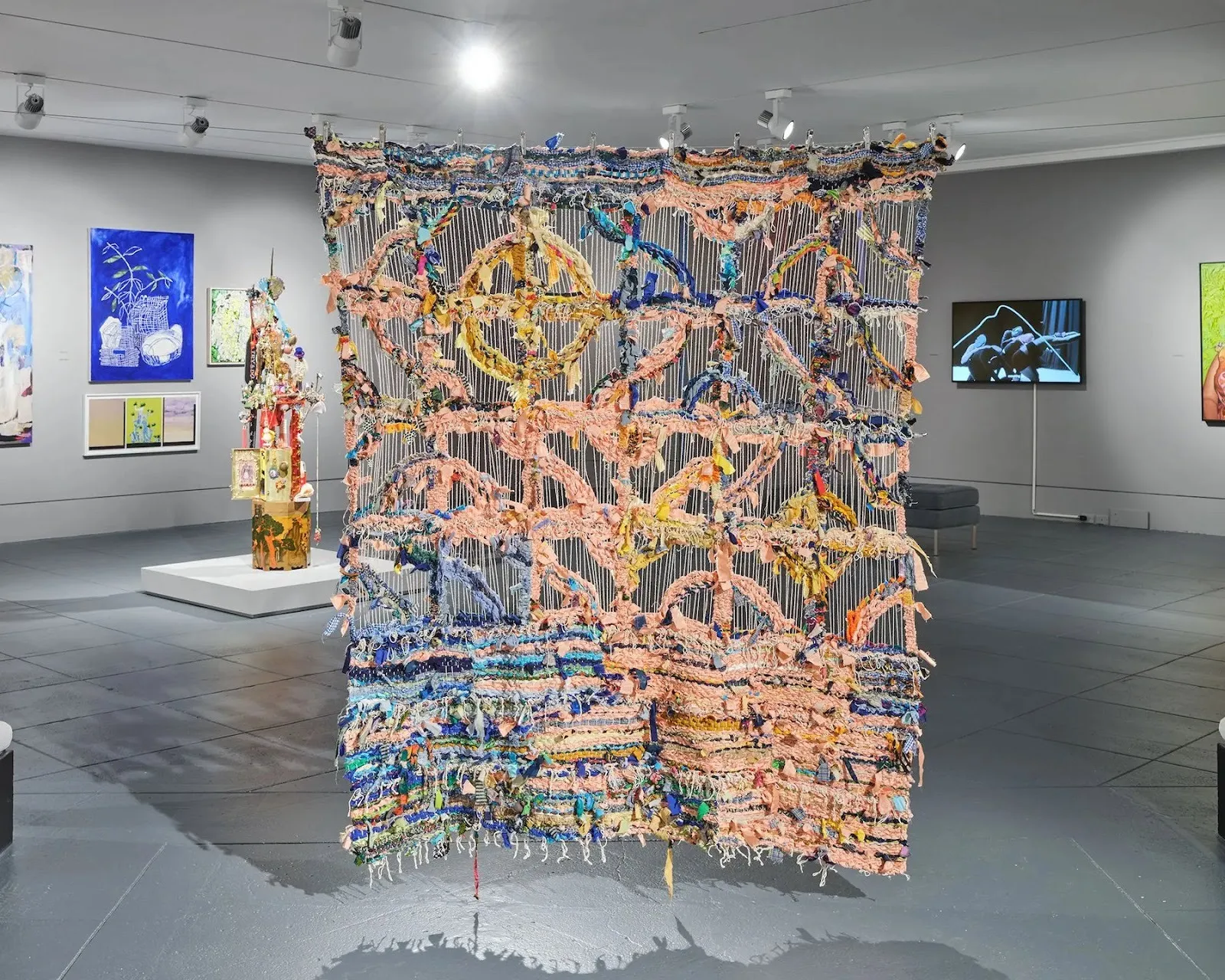 Suspended mixed media tapestry evoking Caribbean residential architecture breeze windows, flesh colored and blue textile hanging from Museum ceiling, the Brooklyn artists exhibition, impulse Magazine review.