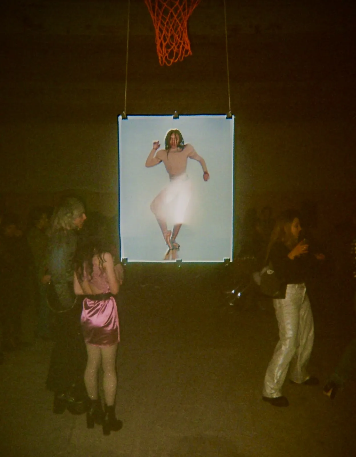 Partygoers standing in front of suspended Valley photograph, underneath basketball net in Bushwick church basement, photographer Nick Brito, performance nonprofit Project iii, stamina dance techno party.