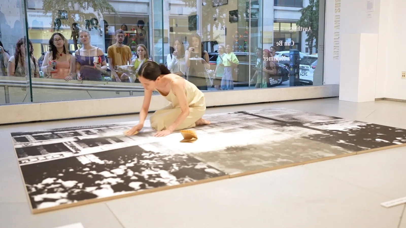 Taiwanese artist ching wei wang kneeling on a large black and white photograph of 228 incident erasing its surface with sandpaper, while audience watch from outside a glass window of parsons school of design gallery.