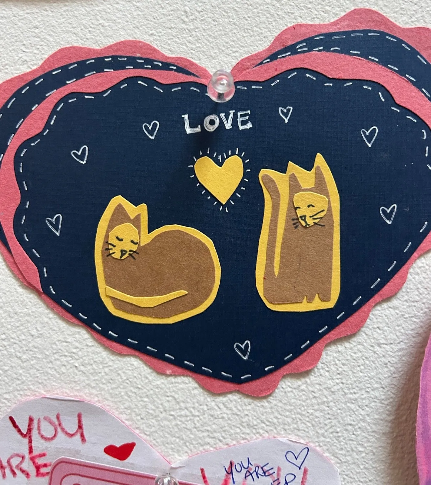 Pink blue and yellow Valentine's Day card with yellow heart and the word love in the middle and two cats cutouts, annual Museum installation at moma ps1 love positive women.