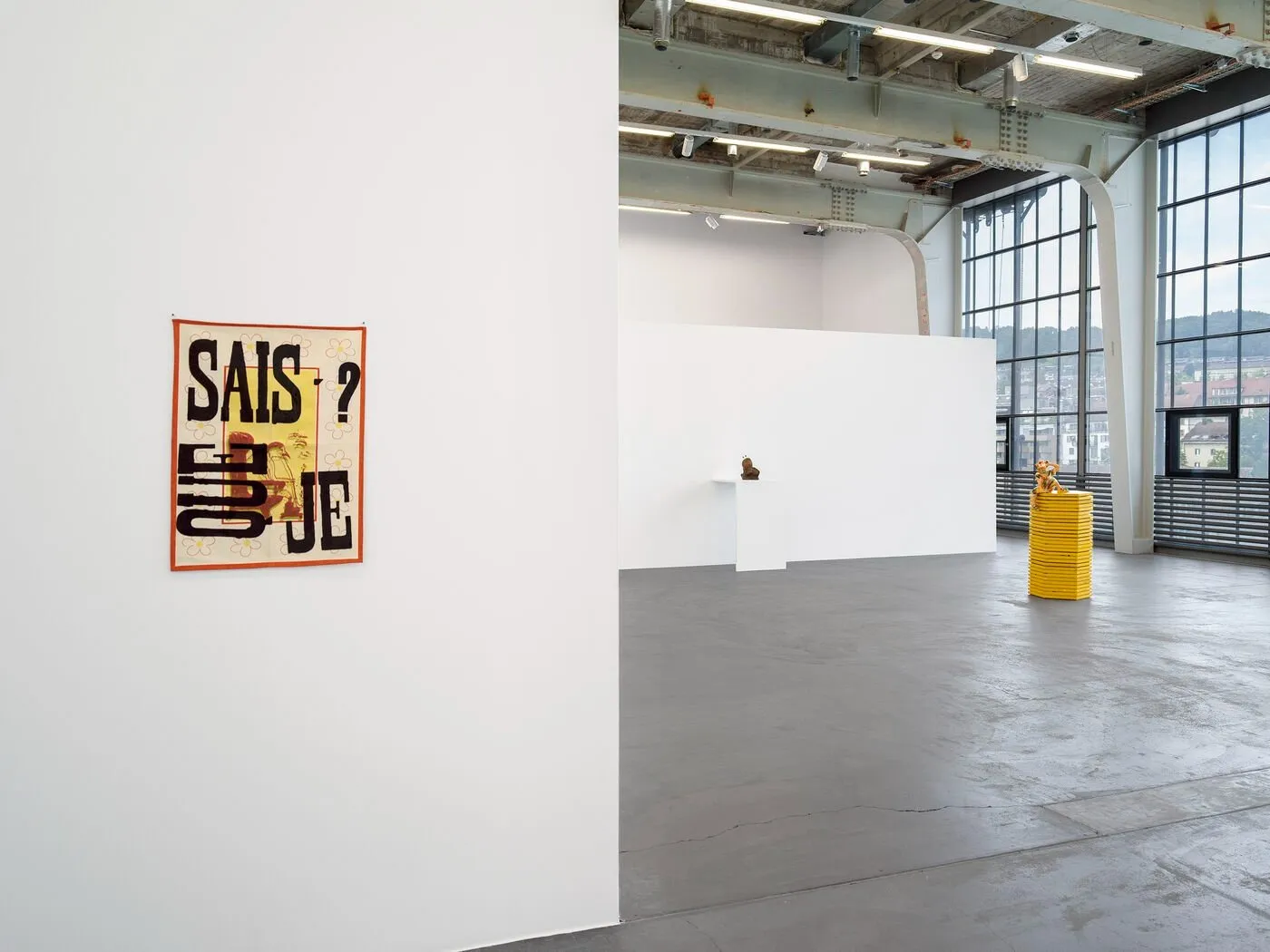 A silkscreen print with que sais-je on white gallery wall, in front of ana jotta's other installation and sculptures as part of composicao at kunsthalle zurich.