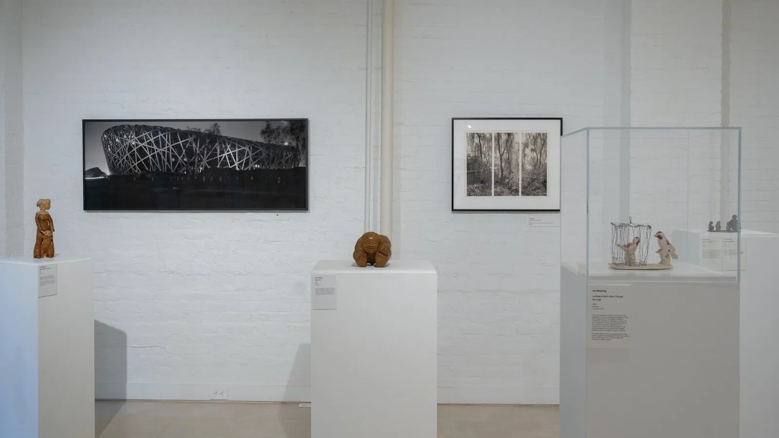 Gallery room with black and white architectural photographs by Lois Conner on wall and figurative sculptures by liu shiming in two-person exhibition beijing stories.