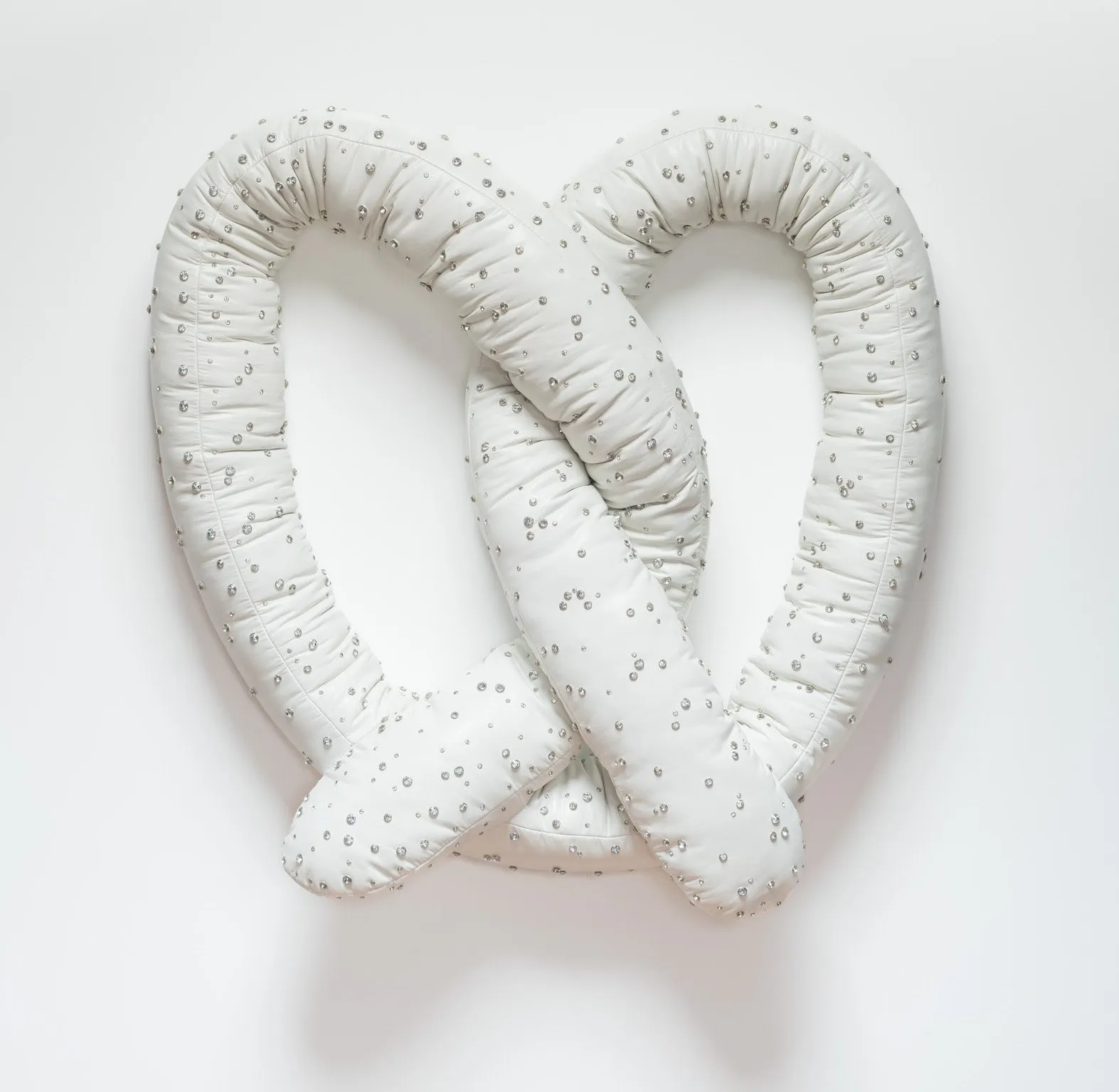 Amanda Ross-Ho, sculpture of soft pretzel with rhinestone beads and soft white fabric hanging on white wall, ily2 gallery presentation at the felix art fair in la.