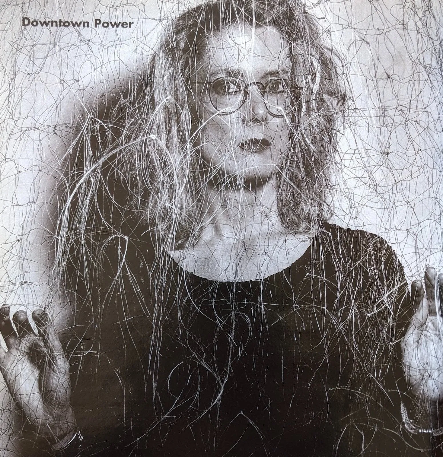 Black and white poster of artist Lesley Dill in front of expressionist gestural abstraction wearing glasses and wearing a black top, text on upper left reads "downtown power".