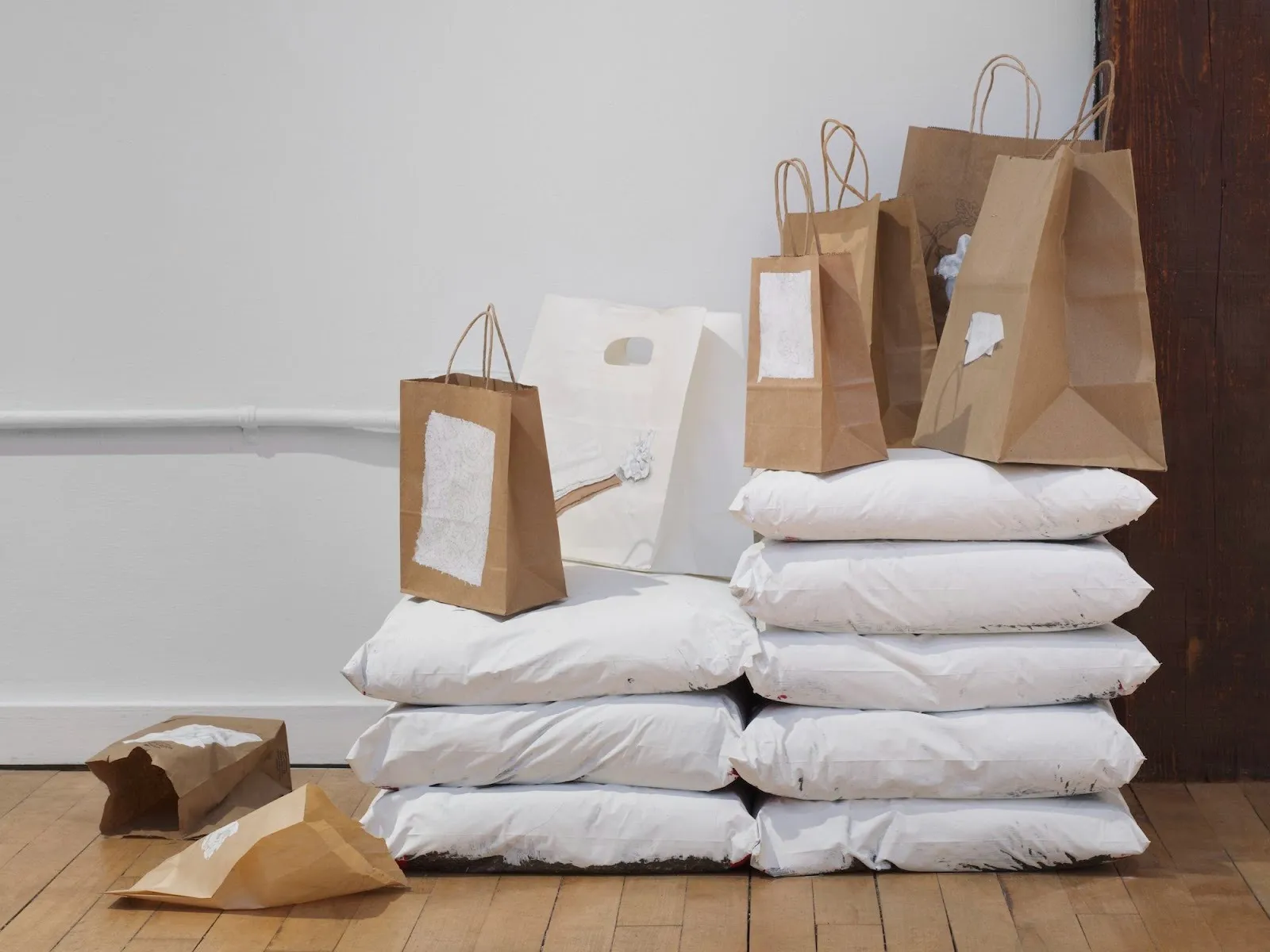 A pile of white sacks and paper bags on wooden floor in front of white wall, kai oh will you marry me installation view.