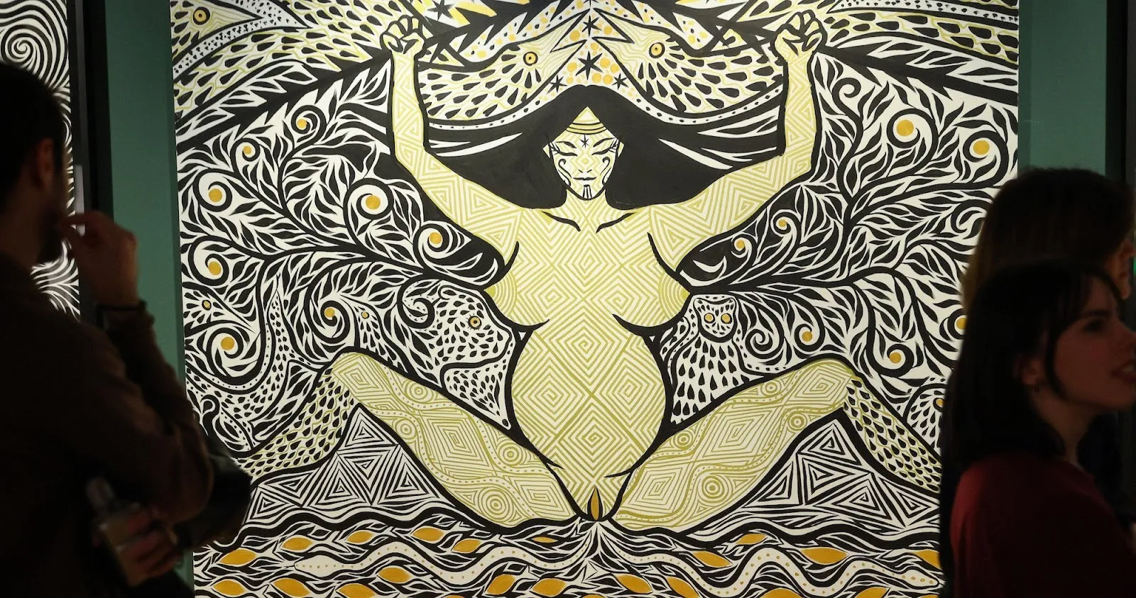 Large-scale mural of indigenous goddess of fertility and life rendered in natural patterns in black, white, and yellow, installation view of amazons, the ancestral future at the contemporary center of culture in barcelona.