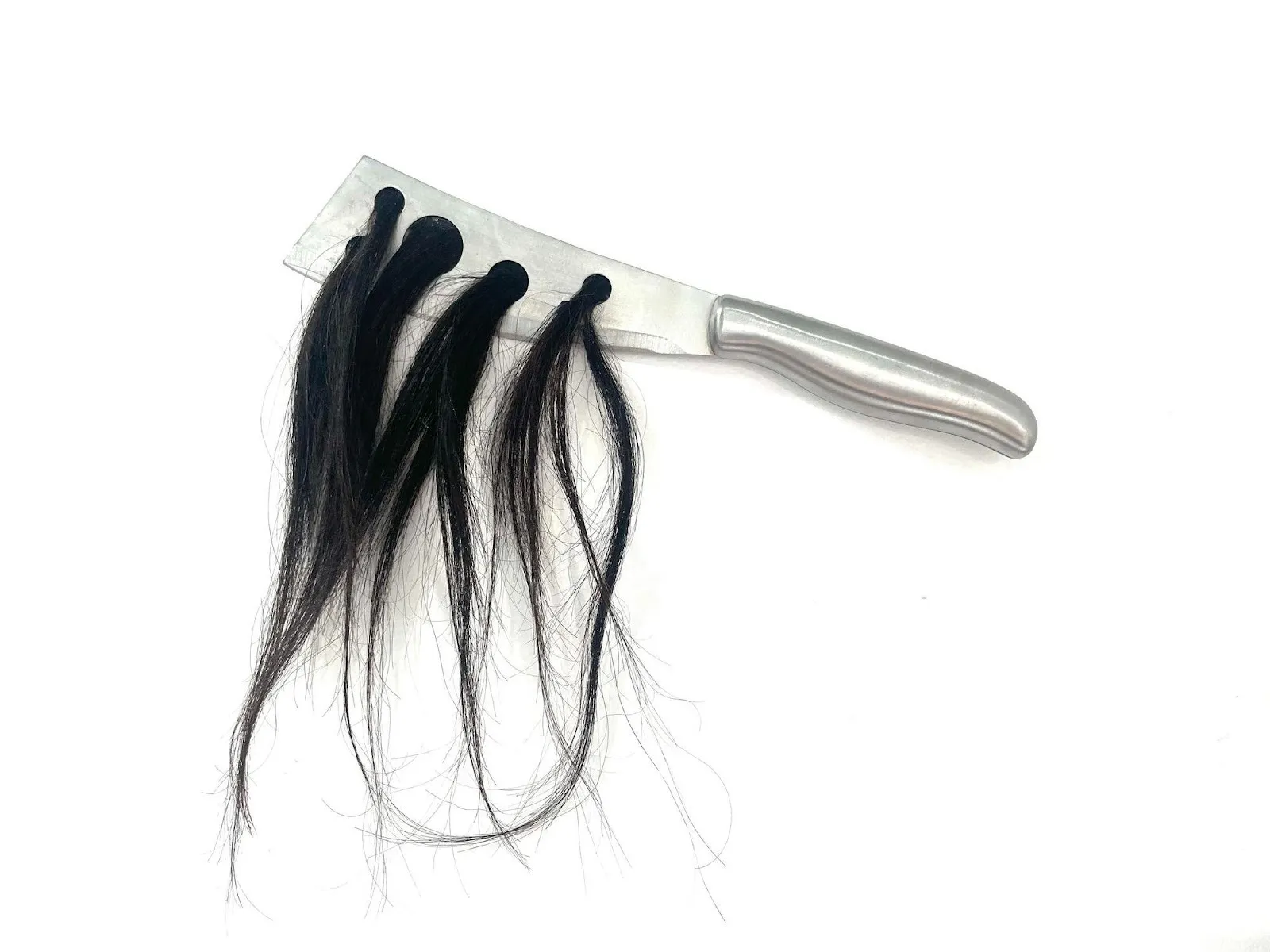 Silver metallic knife with five holes in its blade, one strand of hair coming out of each hole, magdalena dukiewicz object 15, on view as part of care condition control curated by AE chapman at 601artspace.