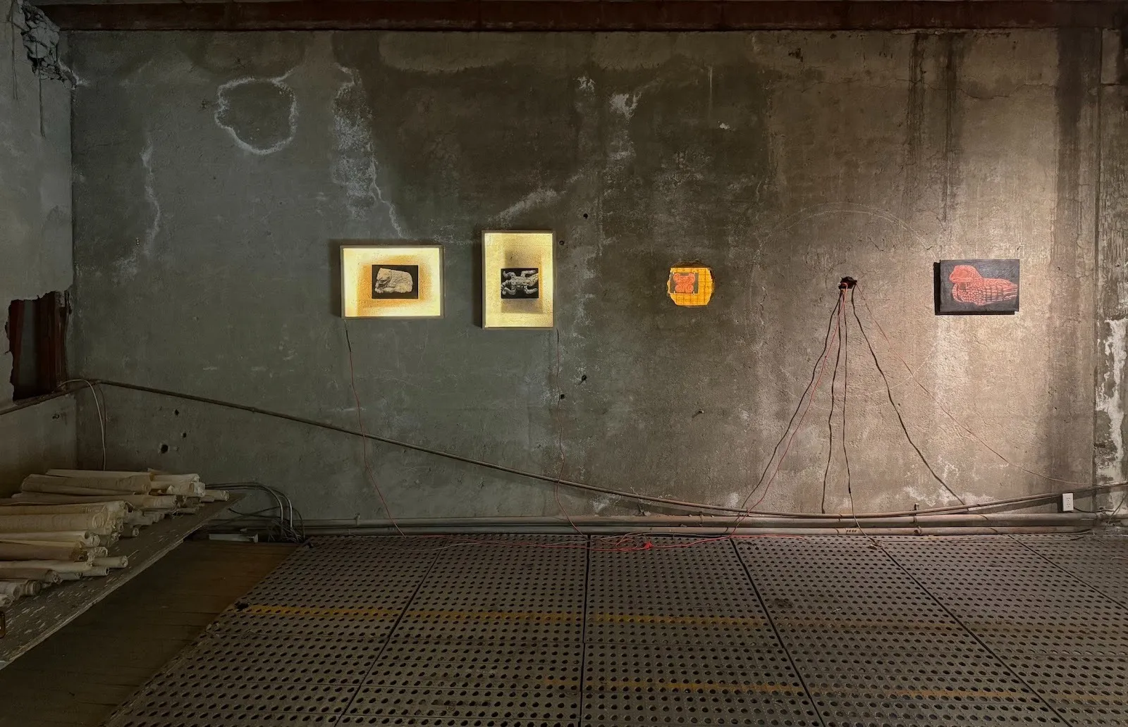 Paintings and multimedia work installed on concrete walls, installation view of peso del peligro at concordia studio, solo exhibition of paulina freifeld.