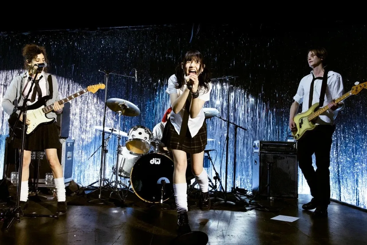 Three young musicians sending on glittery stage, Sharleen Chidiac (guitar), Eva Bella Kaufman (drums), Lia Wang (vocals), Jaxob Eilinghoff (bass) in Anne Imhof’s “DOOM: House of Hope” at Park Avenue Armory.