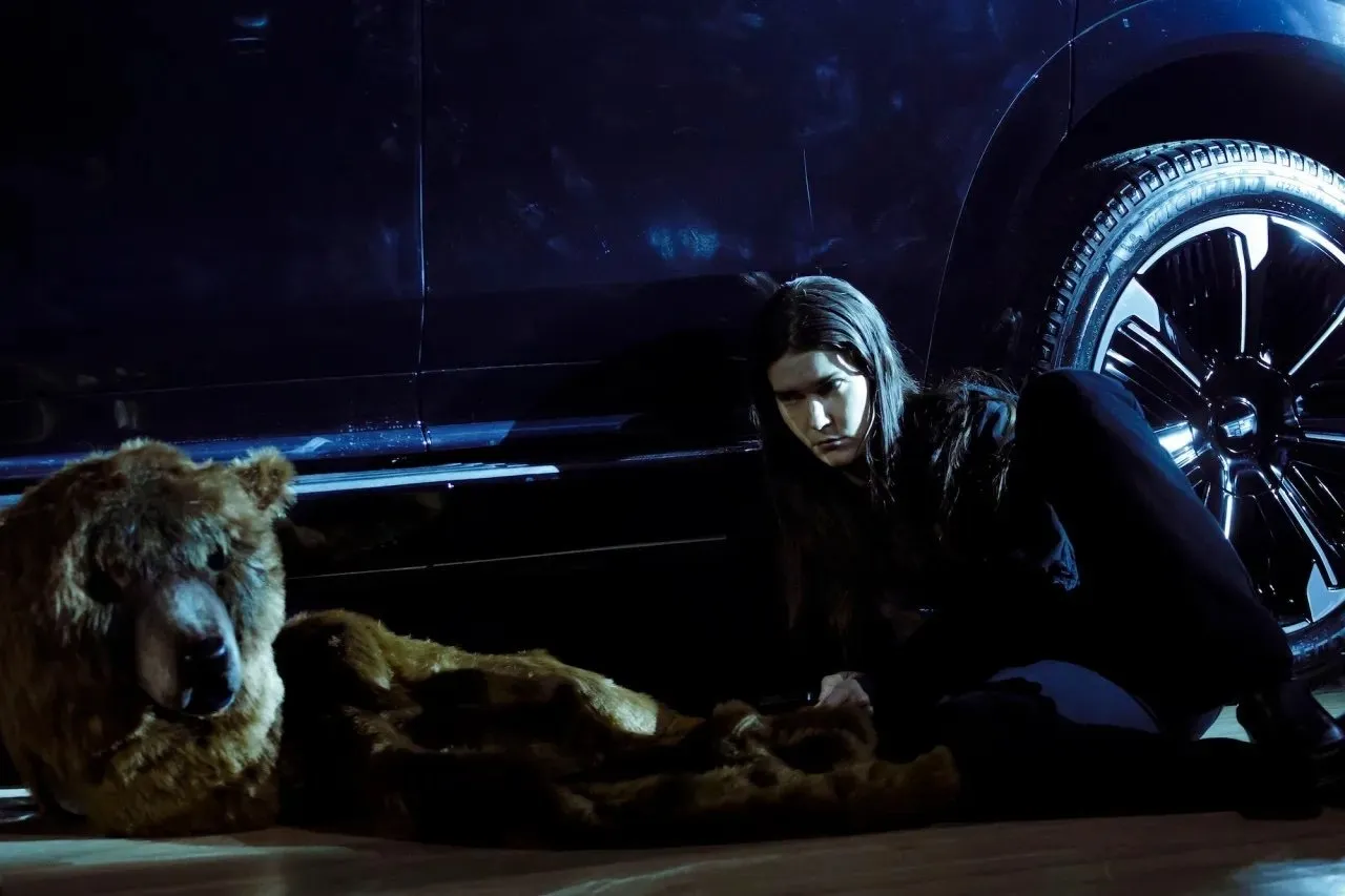 Eliza Douglas on the ground next to a car and a mascot looking intently at the mascot costume, anne imhof, doom house of hope at park avenue armory.