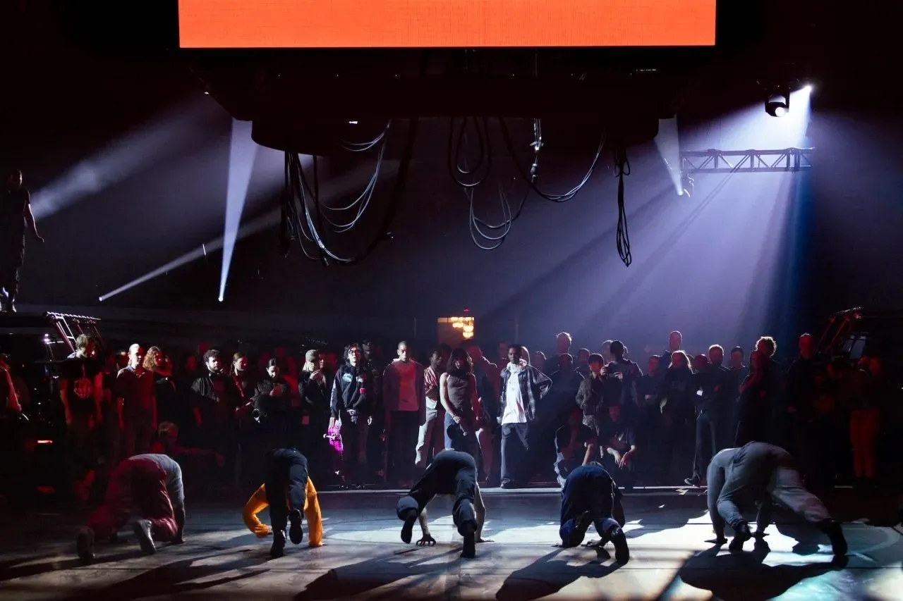 A line of performers crawling on the floor under a dark purplish lighting, Anne Imhof’s “DOOM: House of Hope” at Park Avenue Armory.
