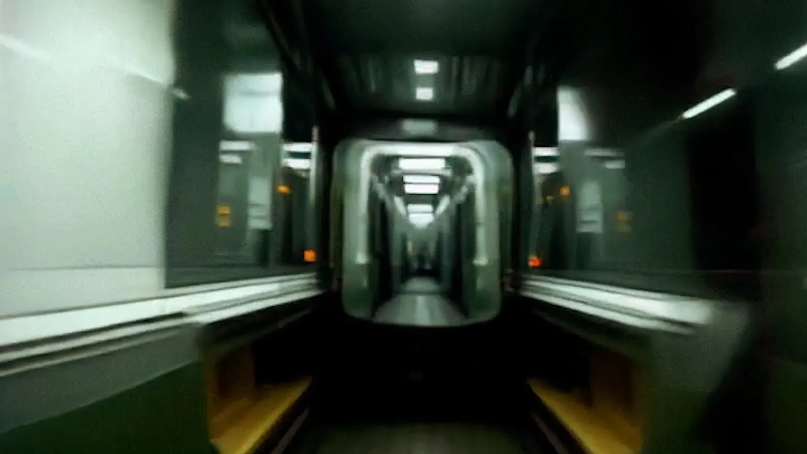 A one-point perspective image of what appears to be a subway track, but there seems to be no door, allowing full viewing access into the subway car as it rushes towards/away from the viewer. The subway station itself is clean and grey/white.