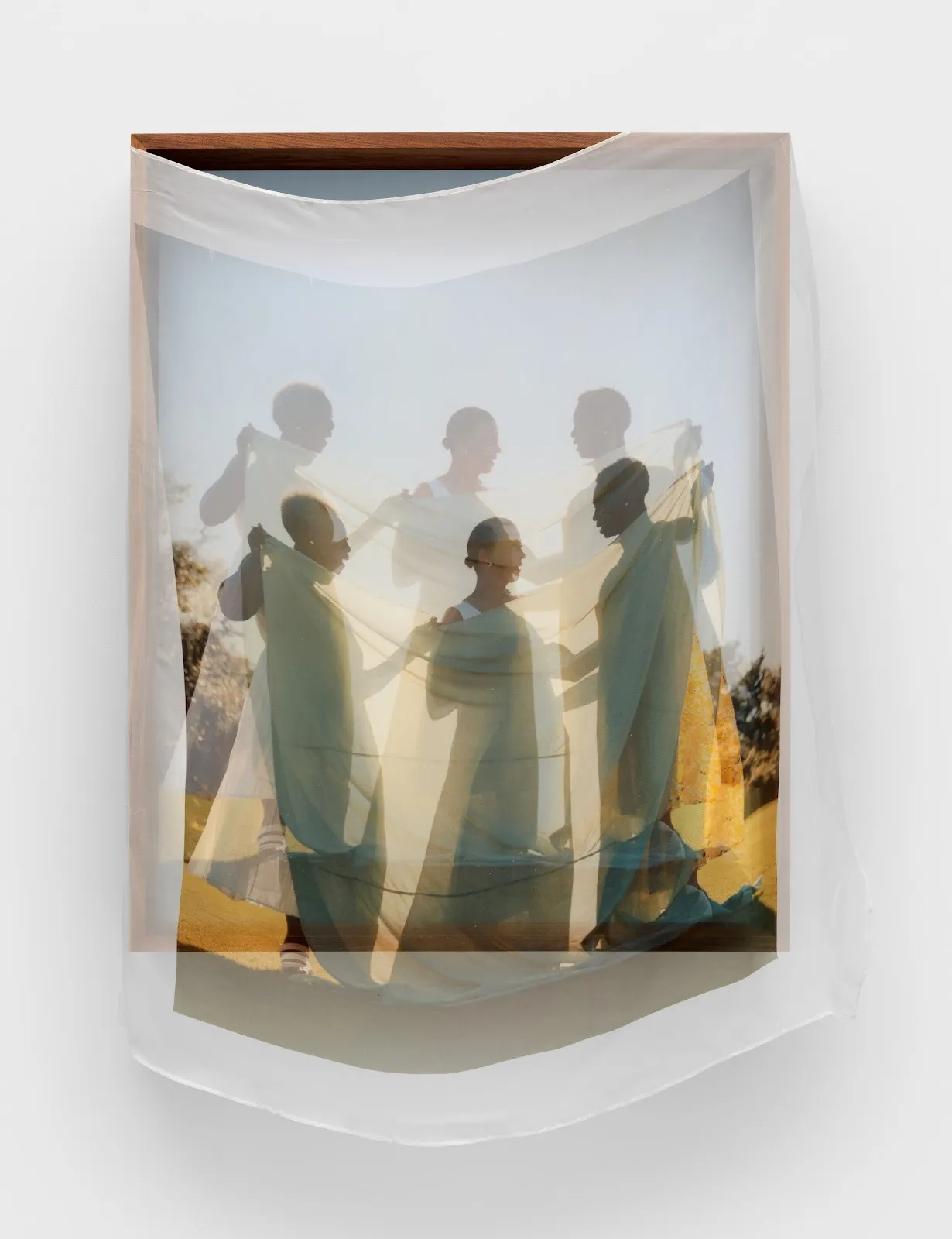 Translucent printed fabric of three people talking with fabric stretched over a printed framed photograph of the same image, Tyler Mitchell, Convivial Conversation, 2024. Dye-sublimation print on fabric, walnut artist's frame.