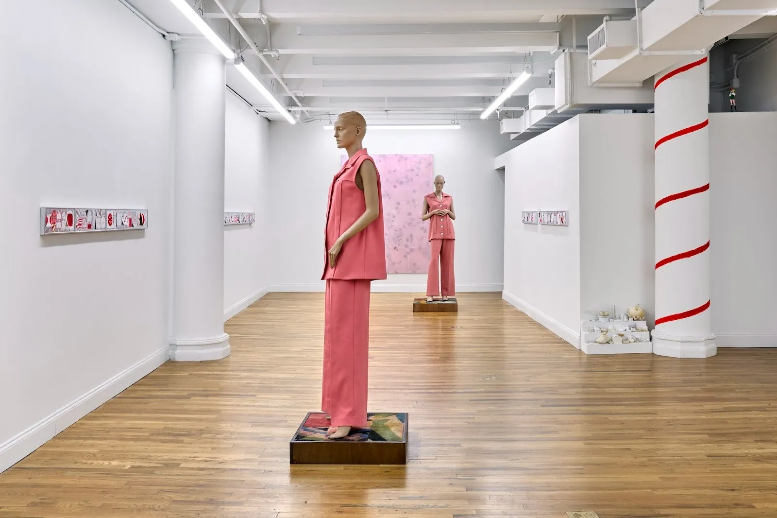 Two mannequins wearing pink suits in the middle of gallery with red drawings and a big pink painting on wall, adam milner meanwhile at rainrain gallery.