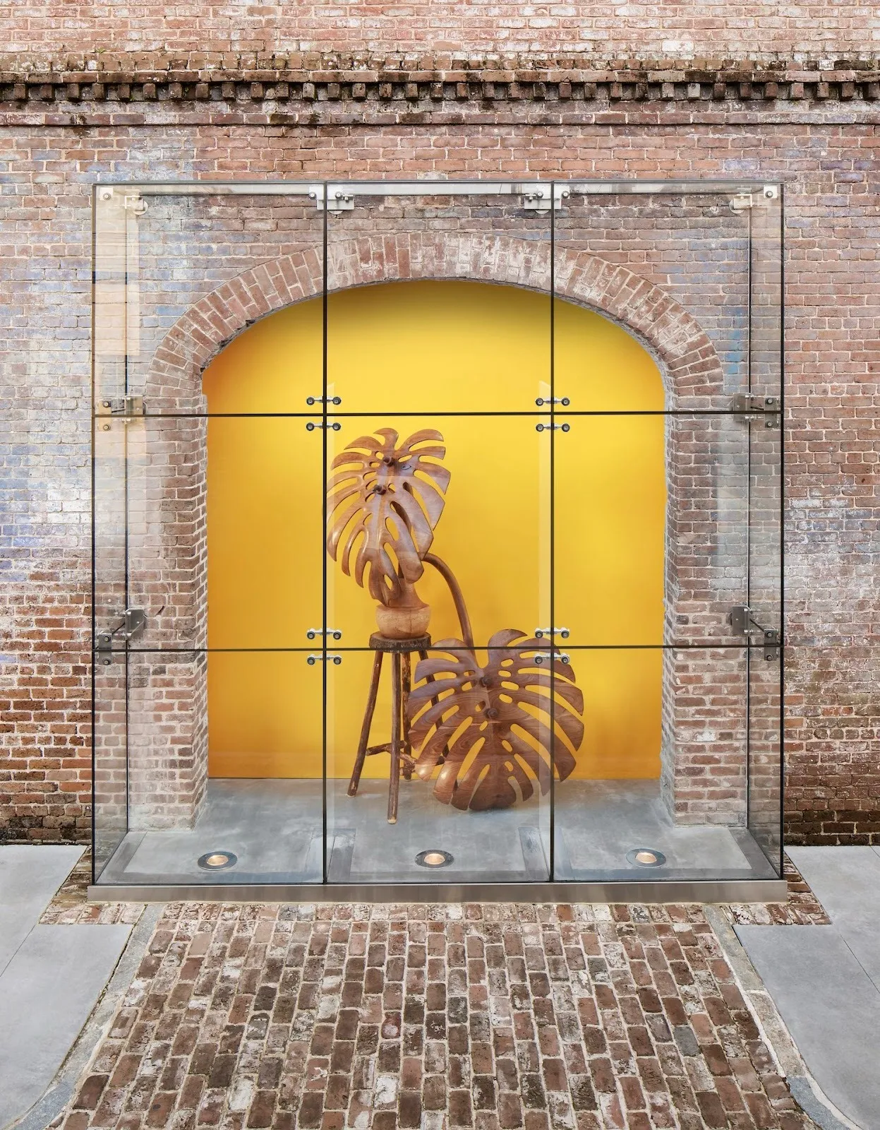 Raul de lara's wooden sculpture in the shape of plant encased within glass cage in front of arch with yellow background, raices/roots at scad museum of art solo exhibition.